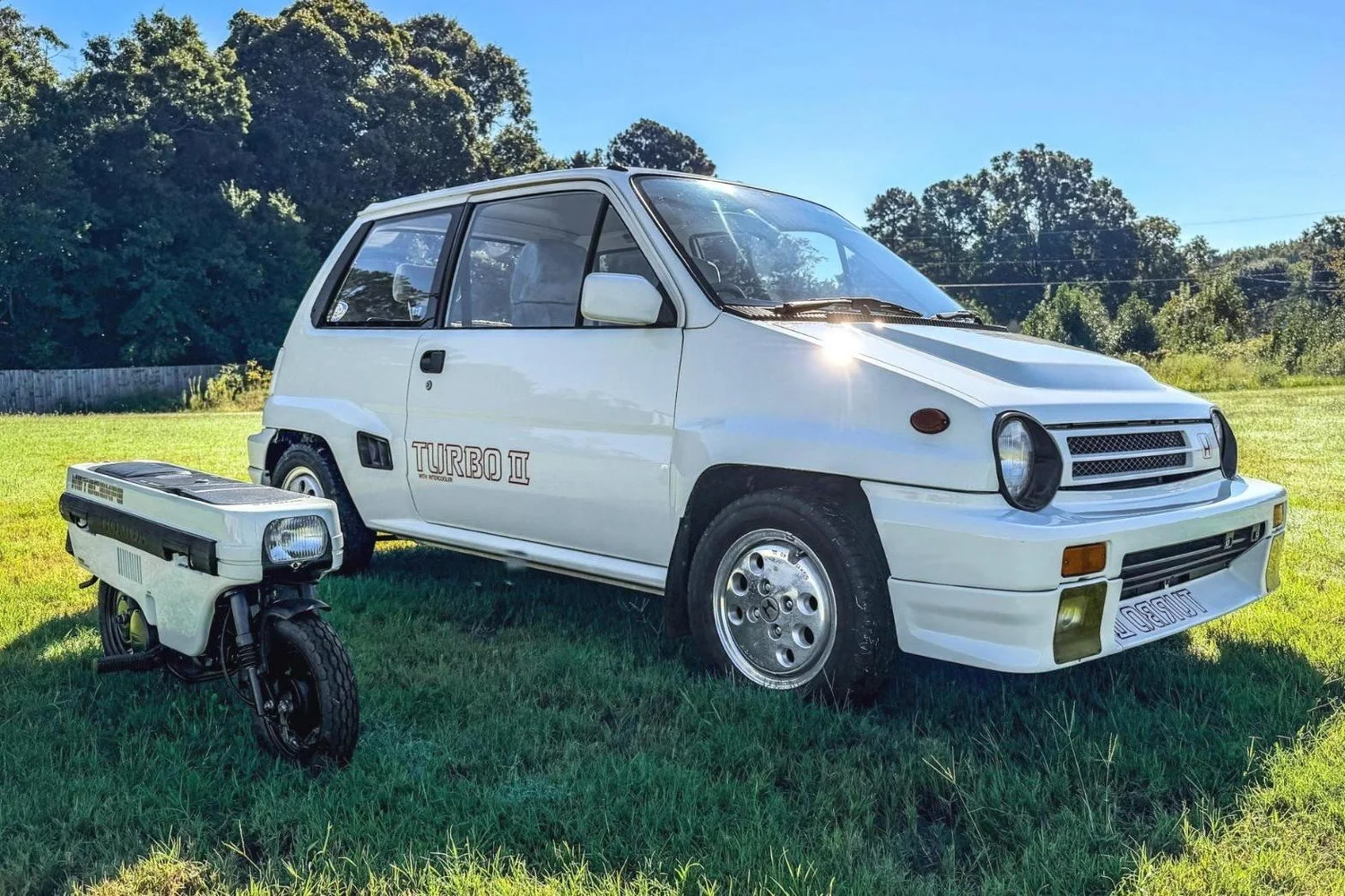 White 1984 Honda City Turbo II parked on grass next to its matching Honda Motocompo folding scooter