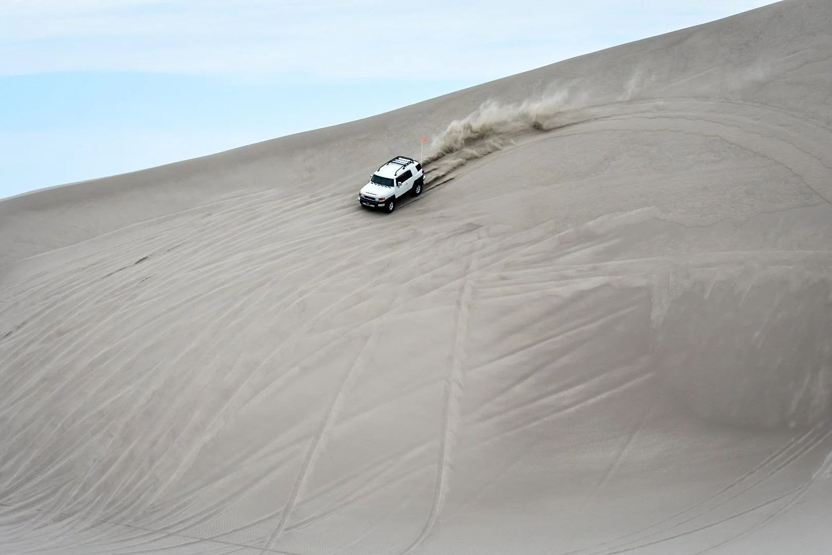 A white SUV driving on sand dunes, kicking up dust behind it.