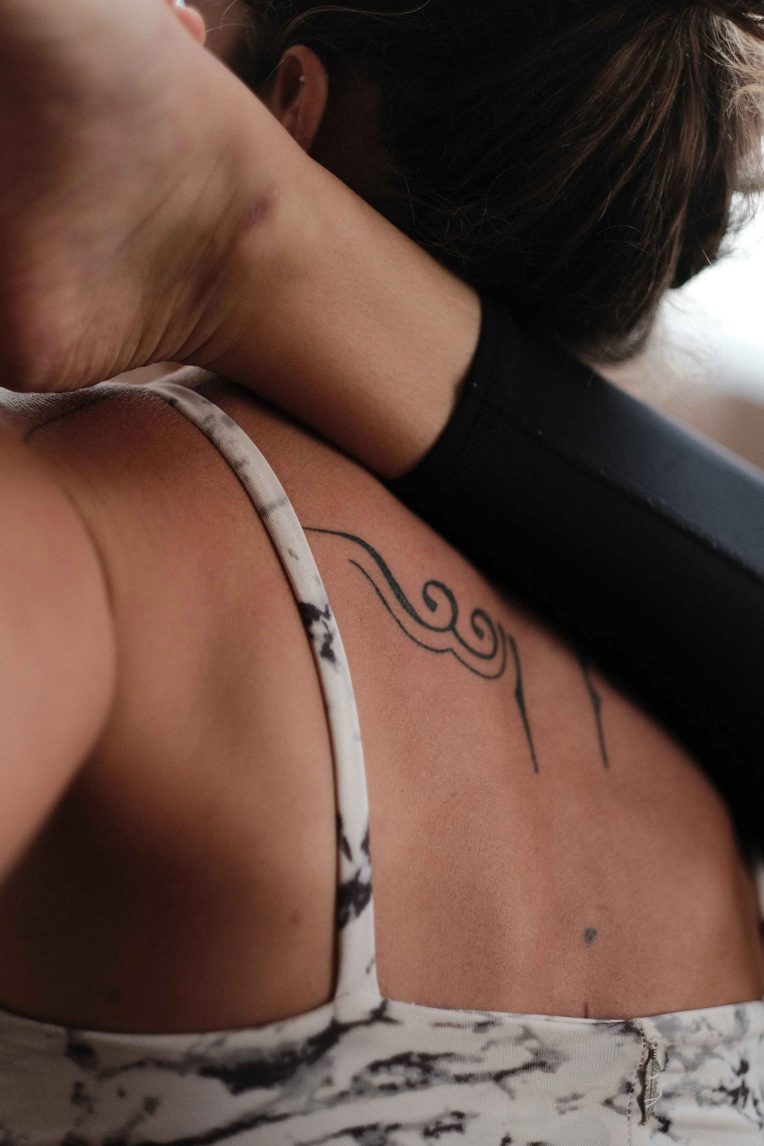 Close-up of a woman lying down, with a tattoo visible on her shoulder, wearing a white and black patterned tank top.