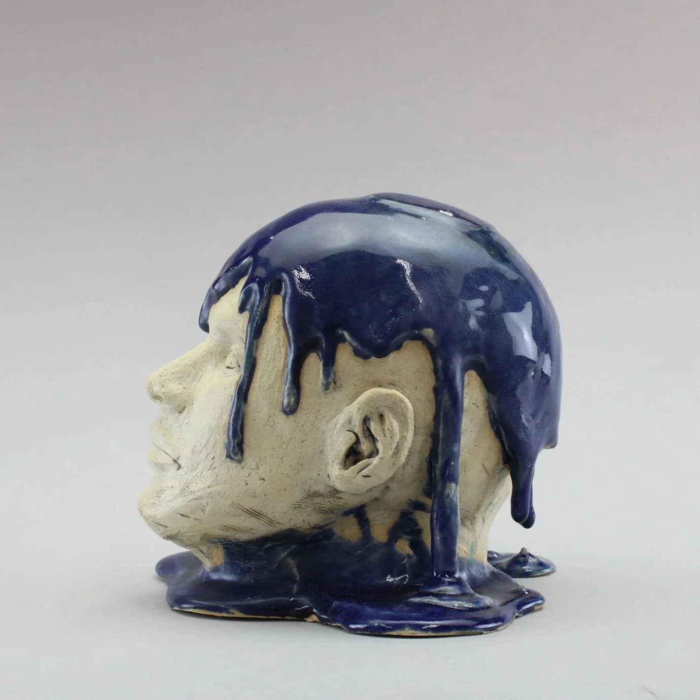 Ceramic sculpture of a man's head with blue glaze dripping over top and down the sides, by Anna Ford.