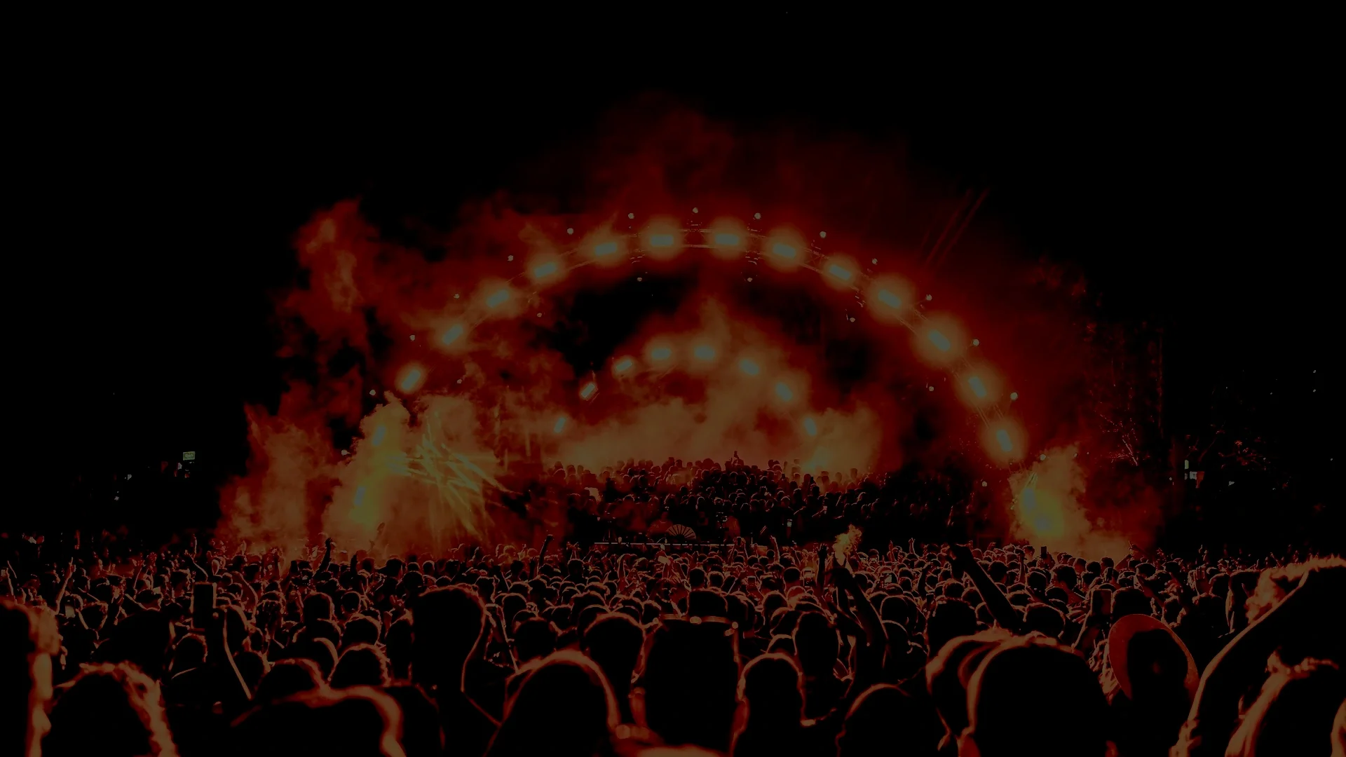 A large crowd at night watching a fireworks display with bright lights, smoke, and sparks in the sky.