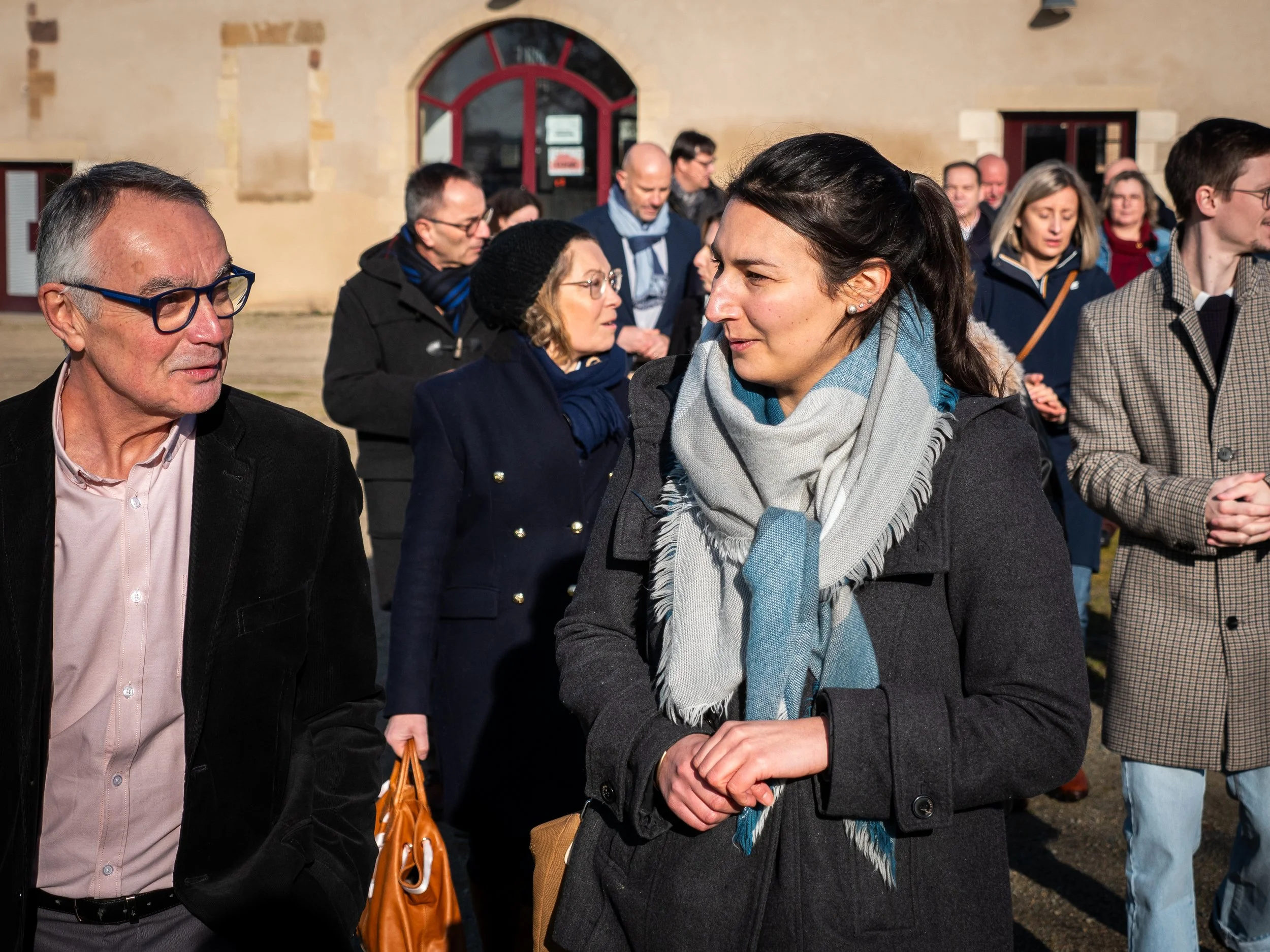 Des personnes discutent lors d'un événement en plein air, avec un bâtiment en pierre en arrière-plan.