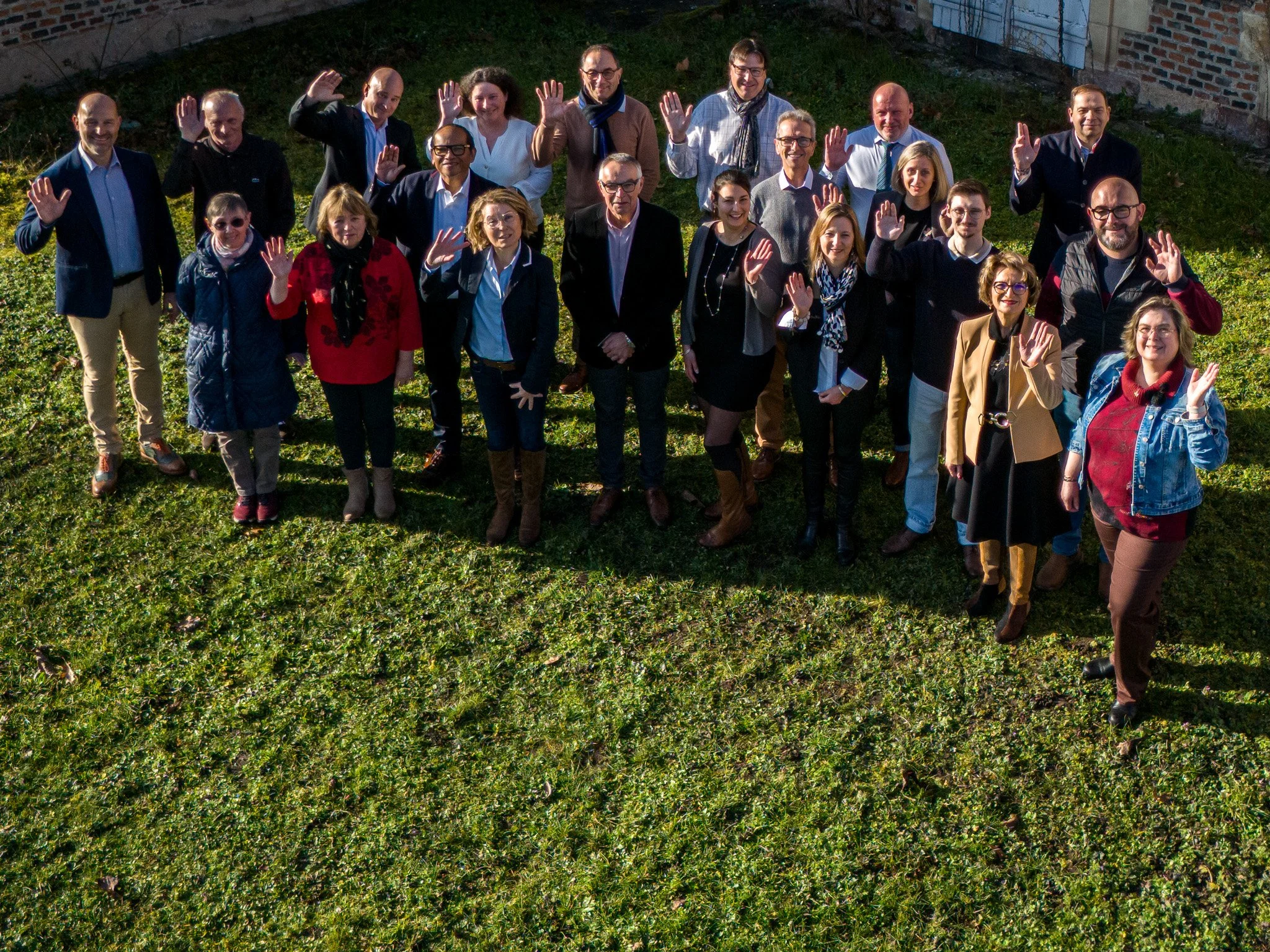 Groupe de personnes posant dans un champ, levant la main en signe de salutation, en extérieur.