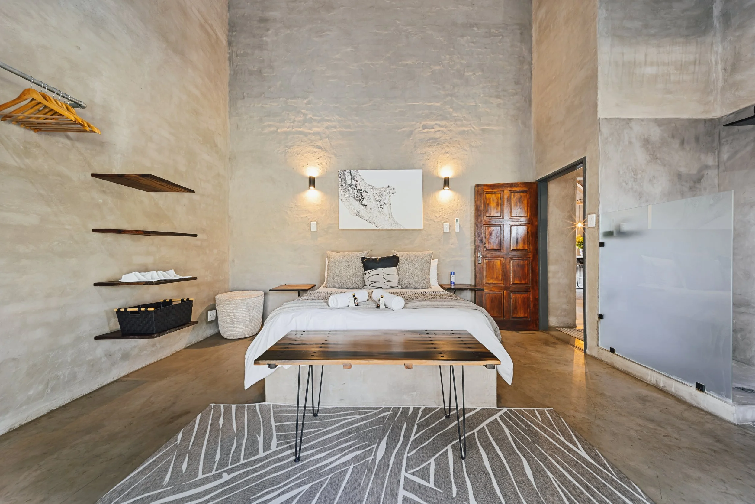 Minimalist bedroom with wooden bed frame, neutral bedding and floating shelves — Moditlo, Greater Kruger.