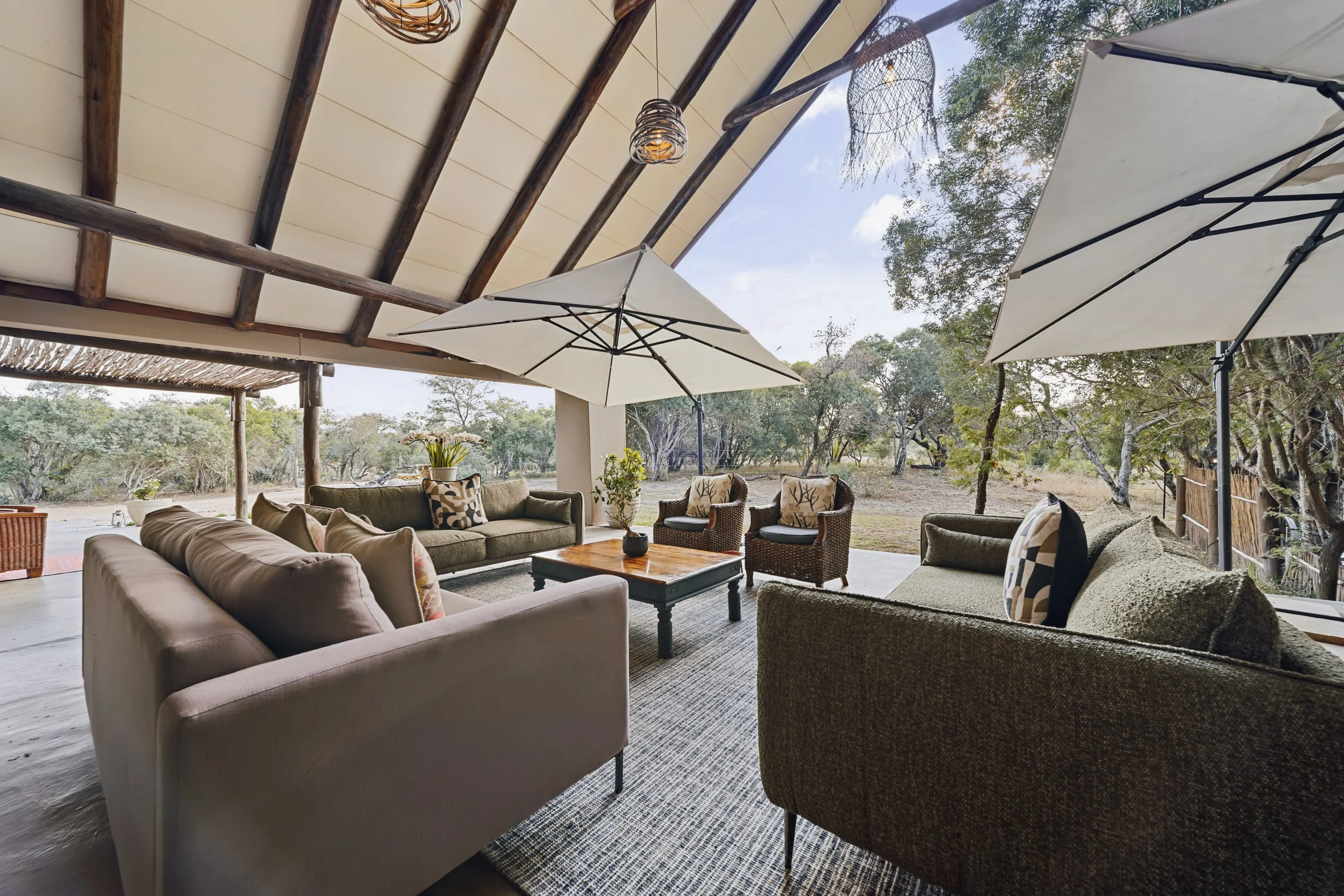 Shaded outdoor lounge with sofas and armchairs under white umbrellas.