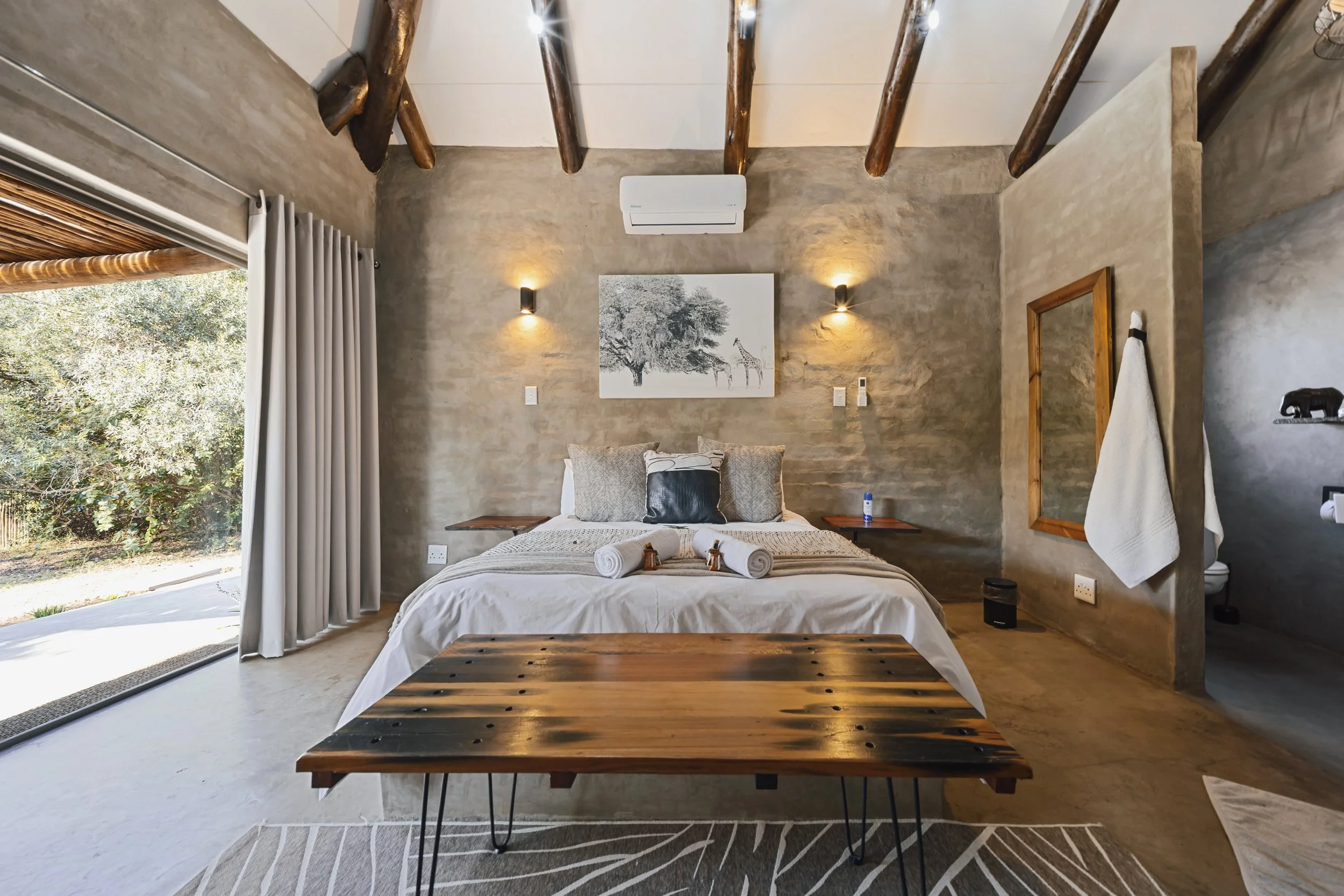 Bedroom with rolled towels, wooden bench and framed giraffe artwork. 