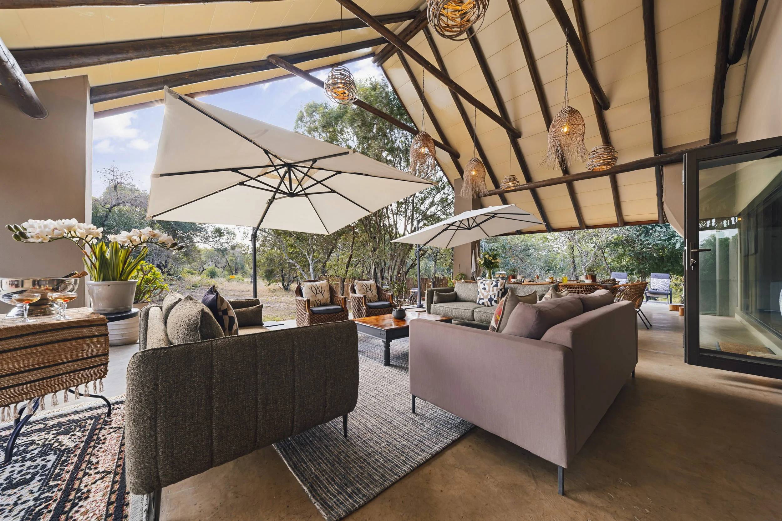 Covered outdoor lounge with woven pendant lights, framed by trees.