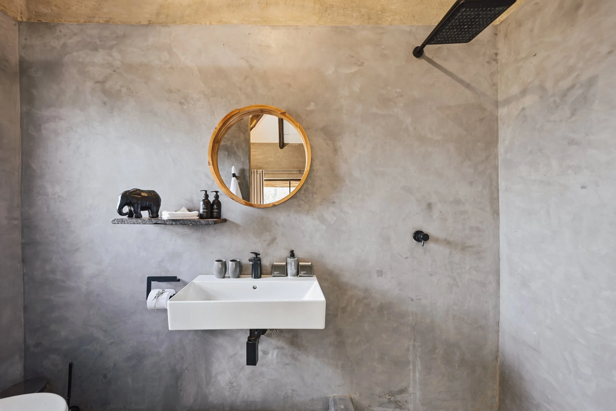 Modern bathroom with concrete wall, ceramic sink and round wood-framed mirror.