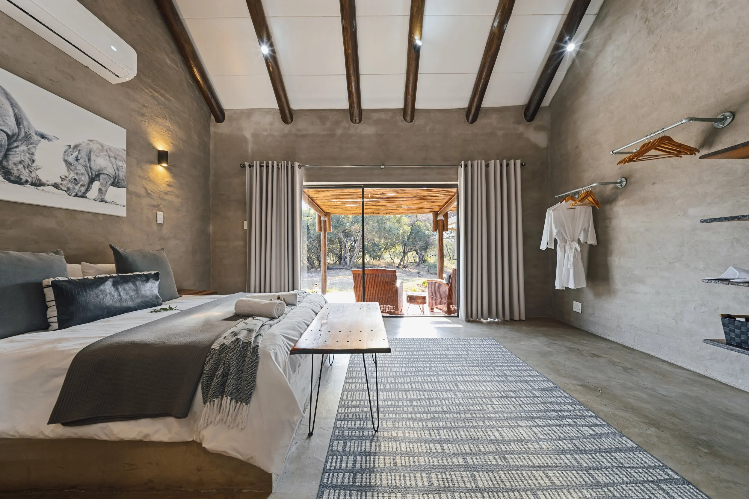 Interior of a bedroom with a bed, wooden ceiling beams, sliding glass door leading to an outdoor patio, wall art with pig illustrations, and curtains.