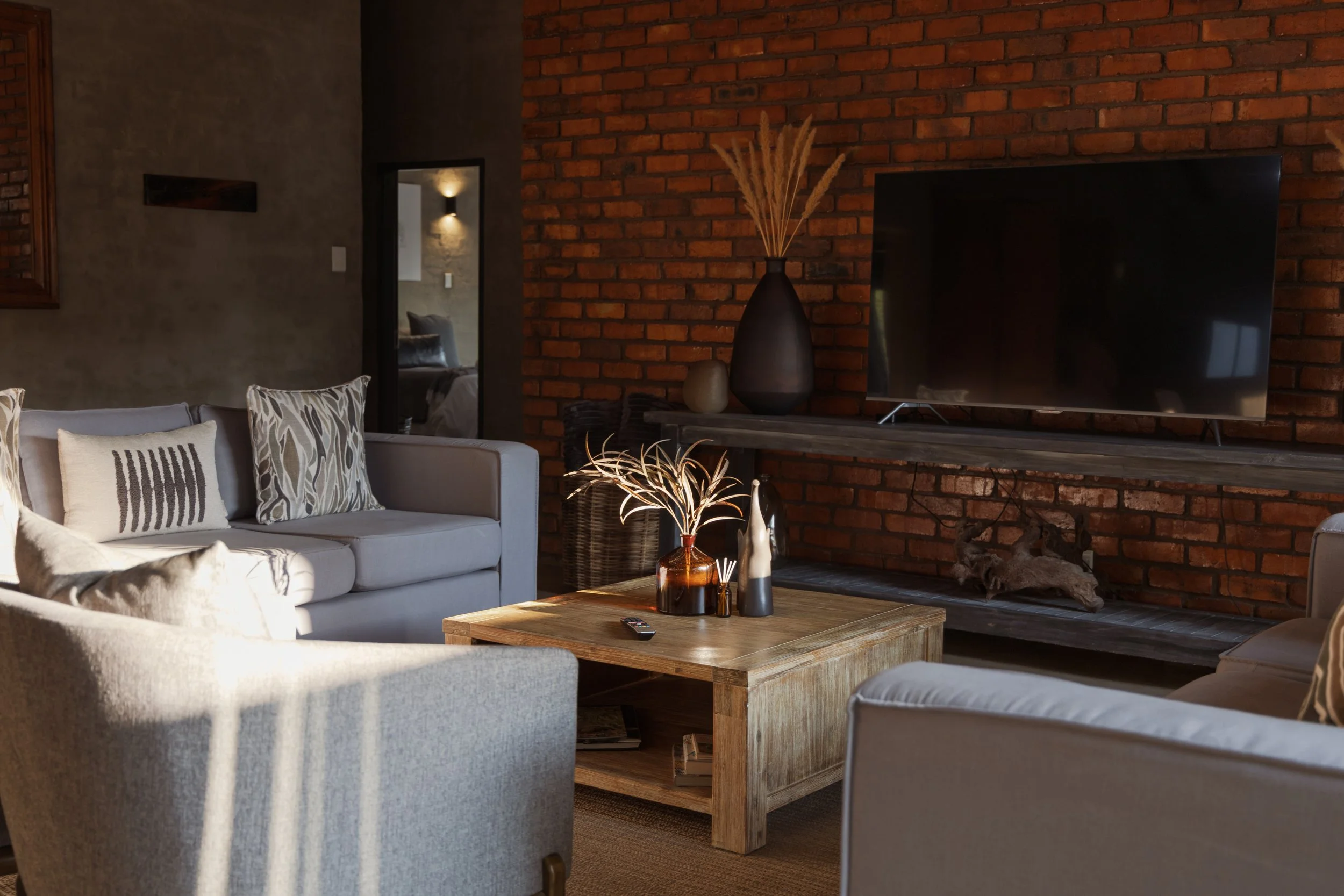 Living room with beige sofa, wooden coffee table and mounted smart TV on a brick wall.
