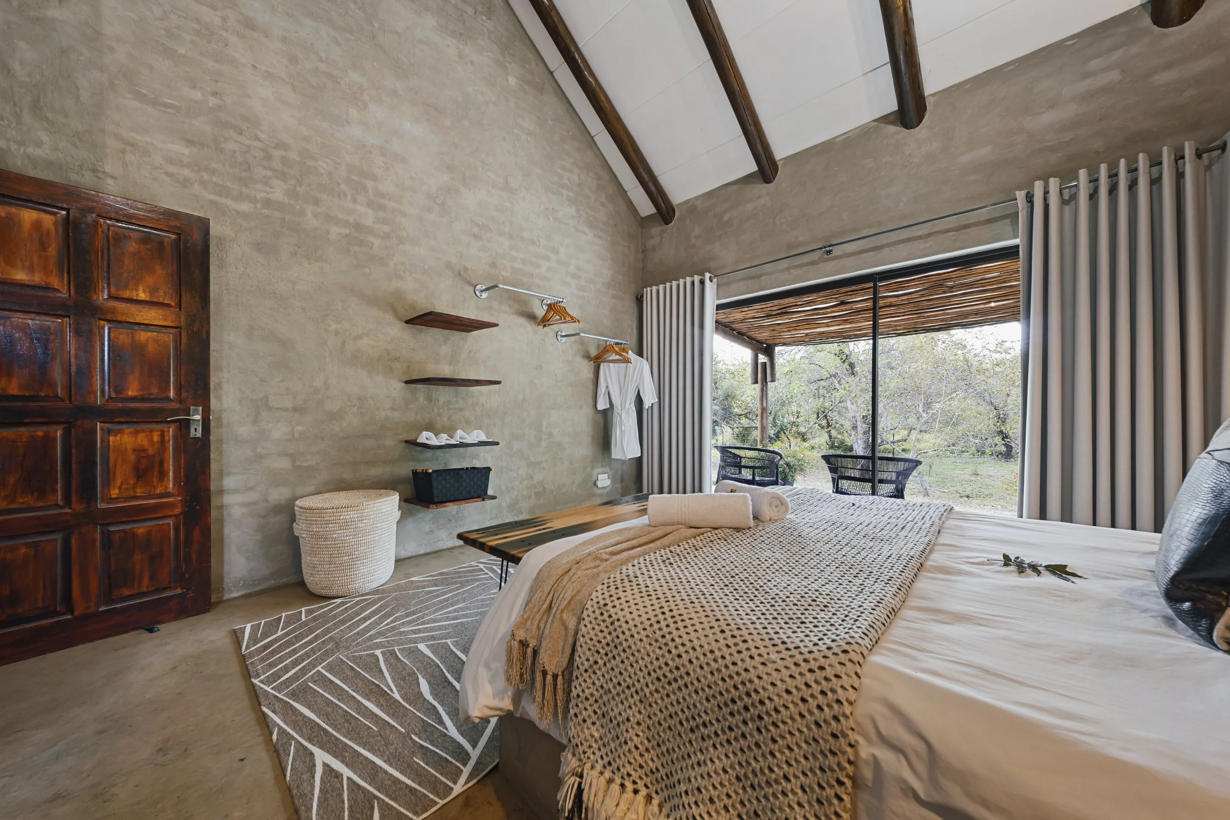 Beige bedroom with beamed ceiling and window onto garden greenery.