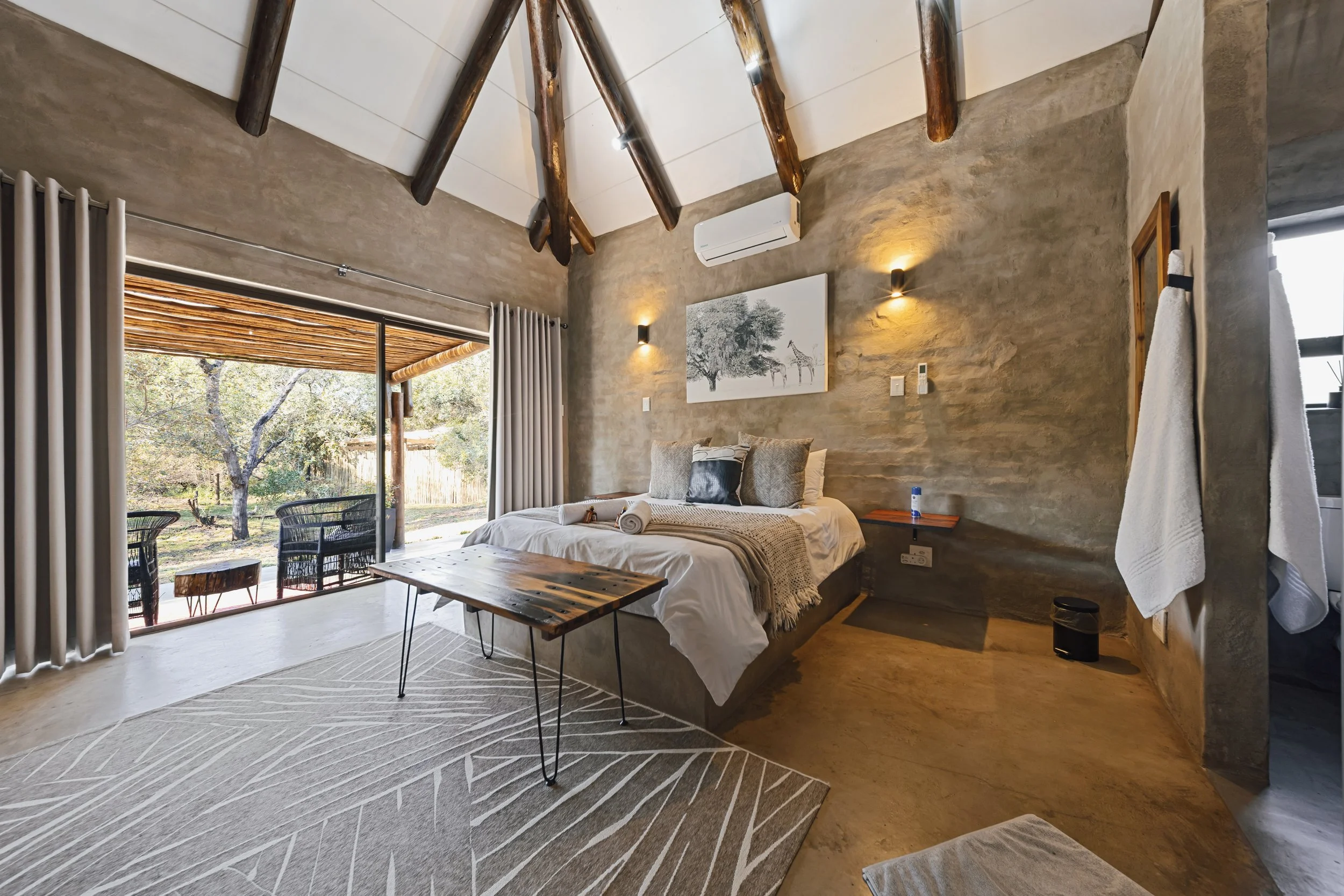 Rustic bedroom with wooden beams and sliding doors to a pergola-shaded deck. 
