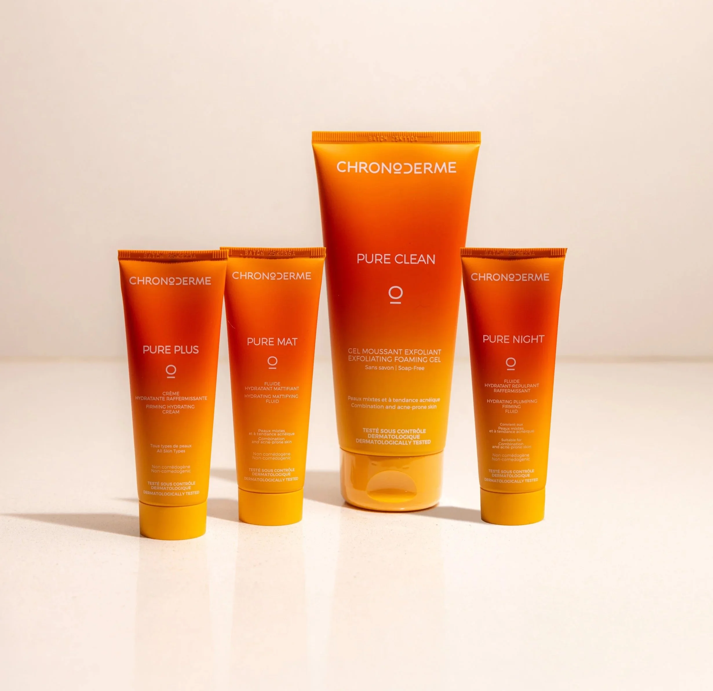 Four orange skincare tubes from the brand Chrono Derme arranged on a white surface. From left to right: Pure Plus, Pure Mat, Pure Clean, and Pure Night.