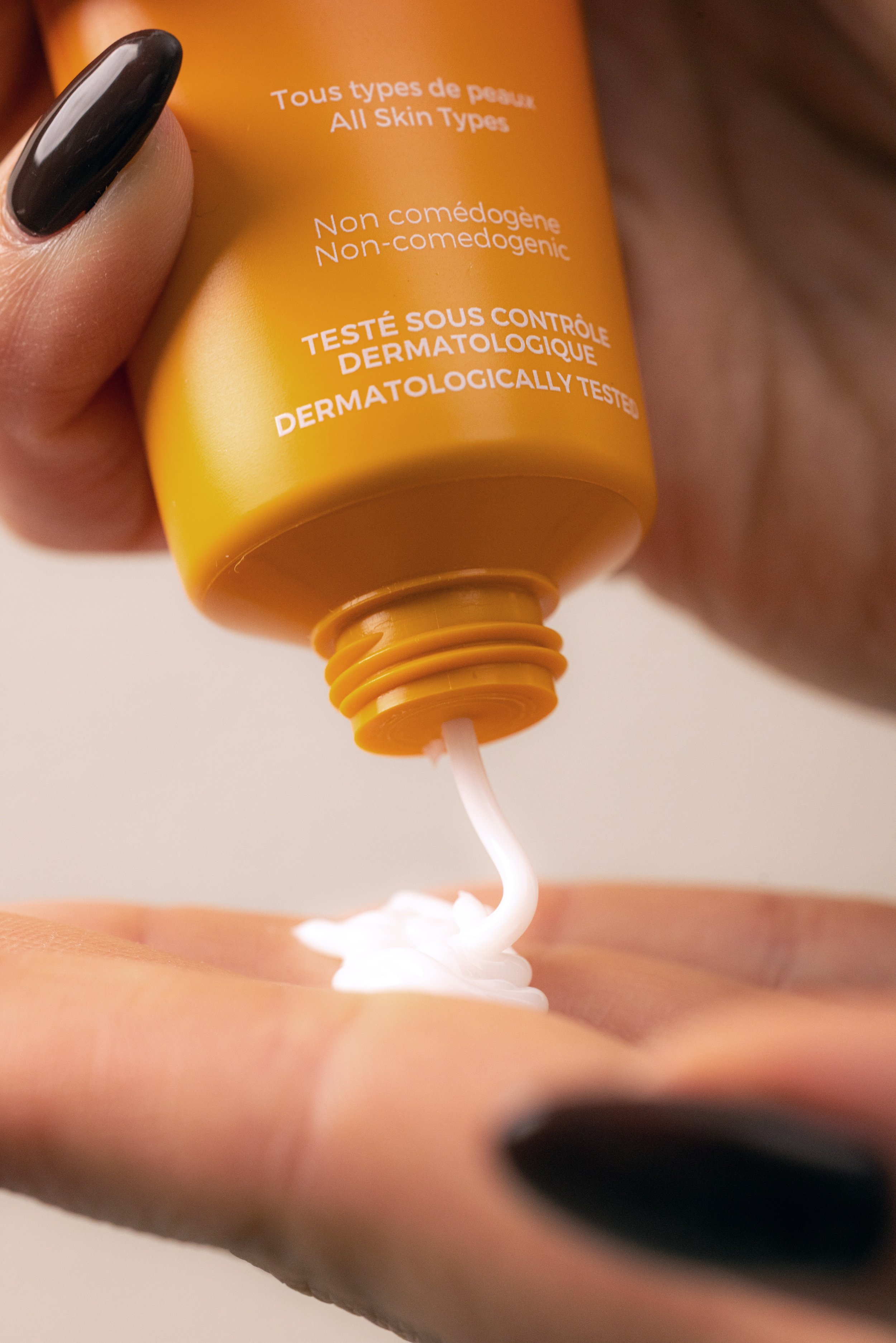 A person squeezing a yellow tube of skin care product onto their hand.