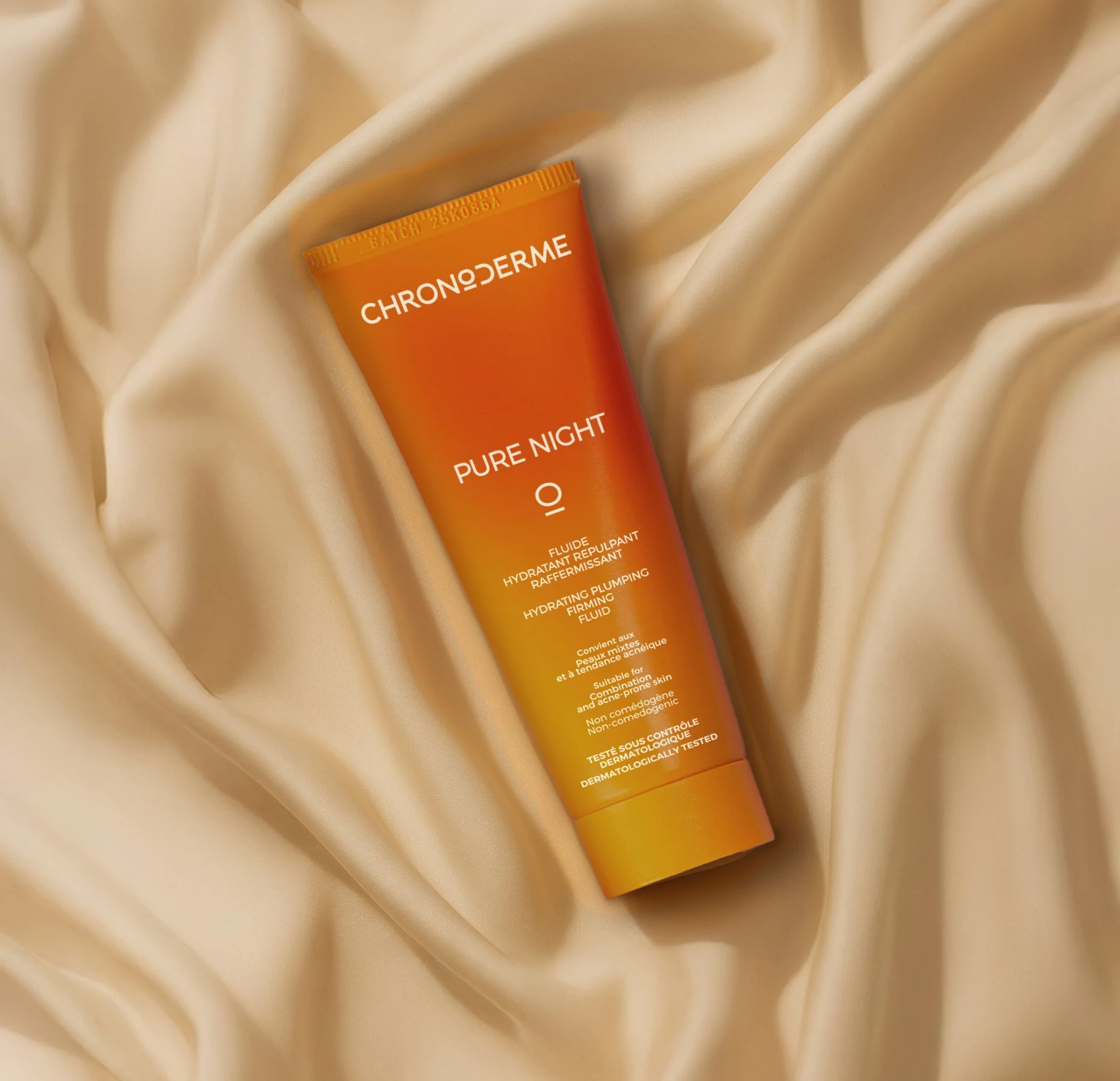 A tube of ChronoDerme Pure Night IO hydrating plumping firming fluid resting on a cream-colored satin fabric.