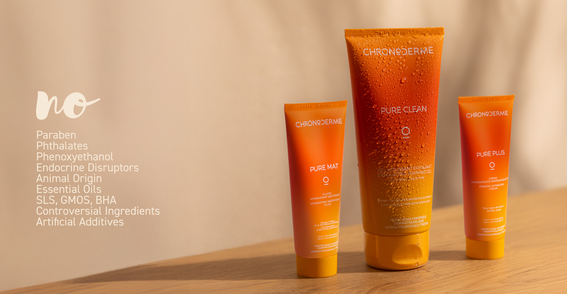 Three orange skincare products from ChronoDerm on a wooden surface, with a beige background. The products include Pure Matte, Pure Clean, and Pure Plus, featuring water droplets on their packaging.