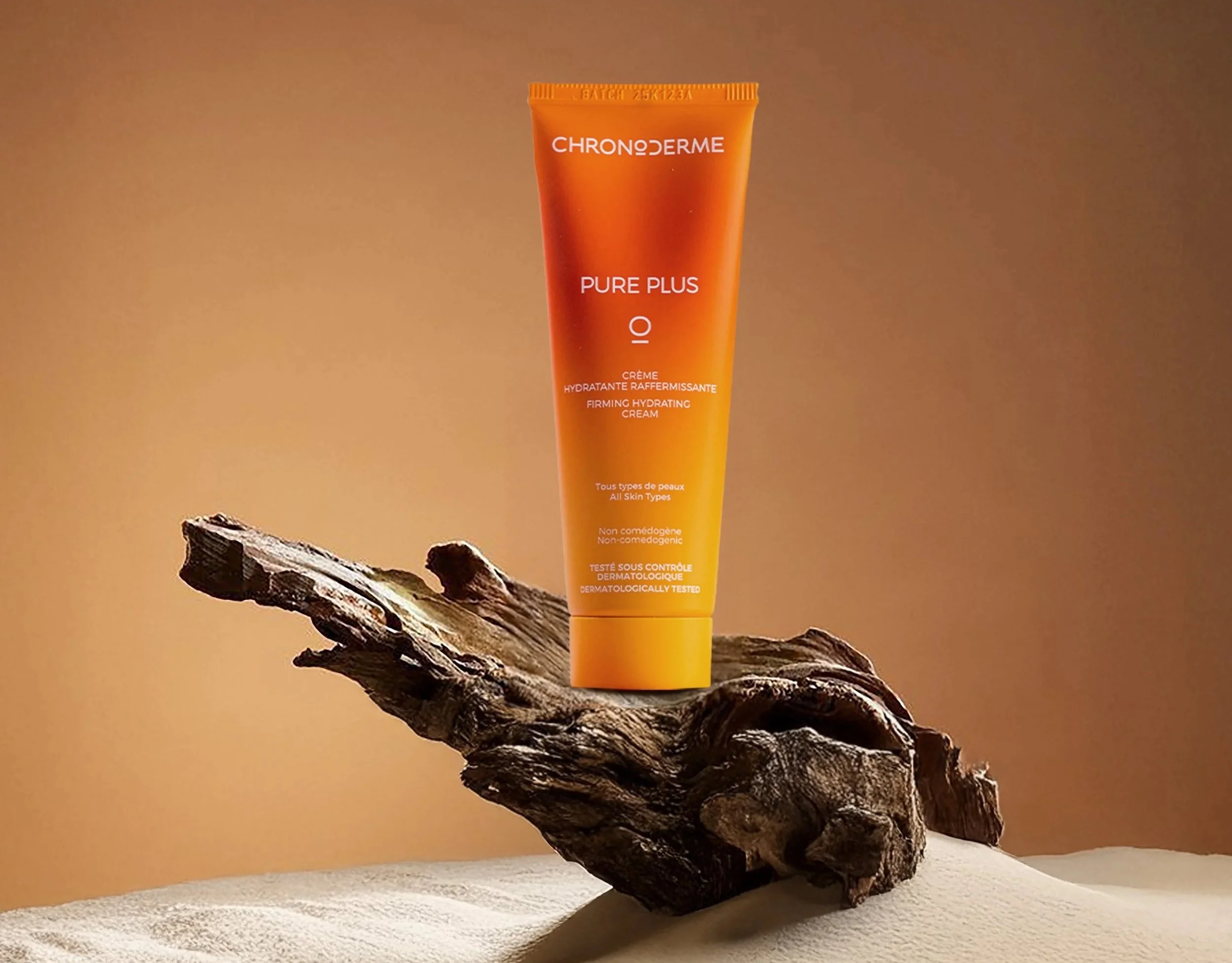 A tube of ChronoDerme Pure Plus IO firming hydrating cream on a piece of wood with a warm beige background.