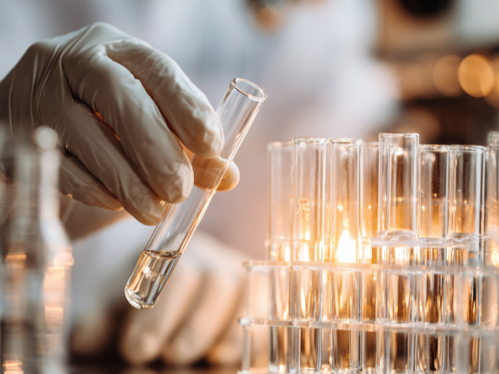 A scientist wearing gloves holding a test tube in a laboratory with test tubes containing liquids.