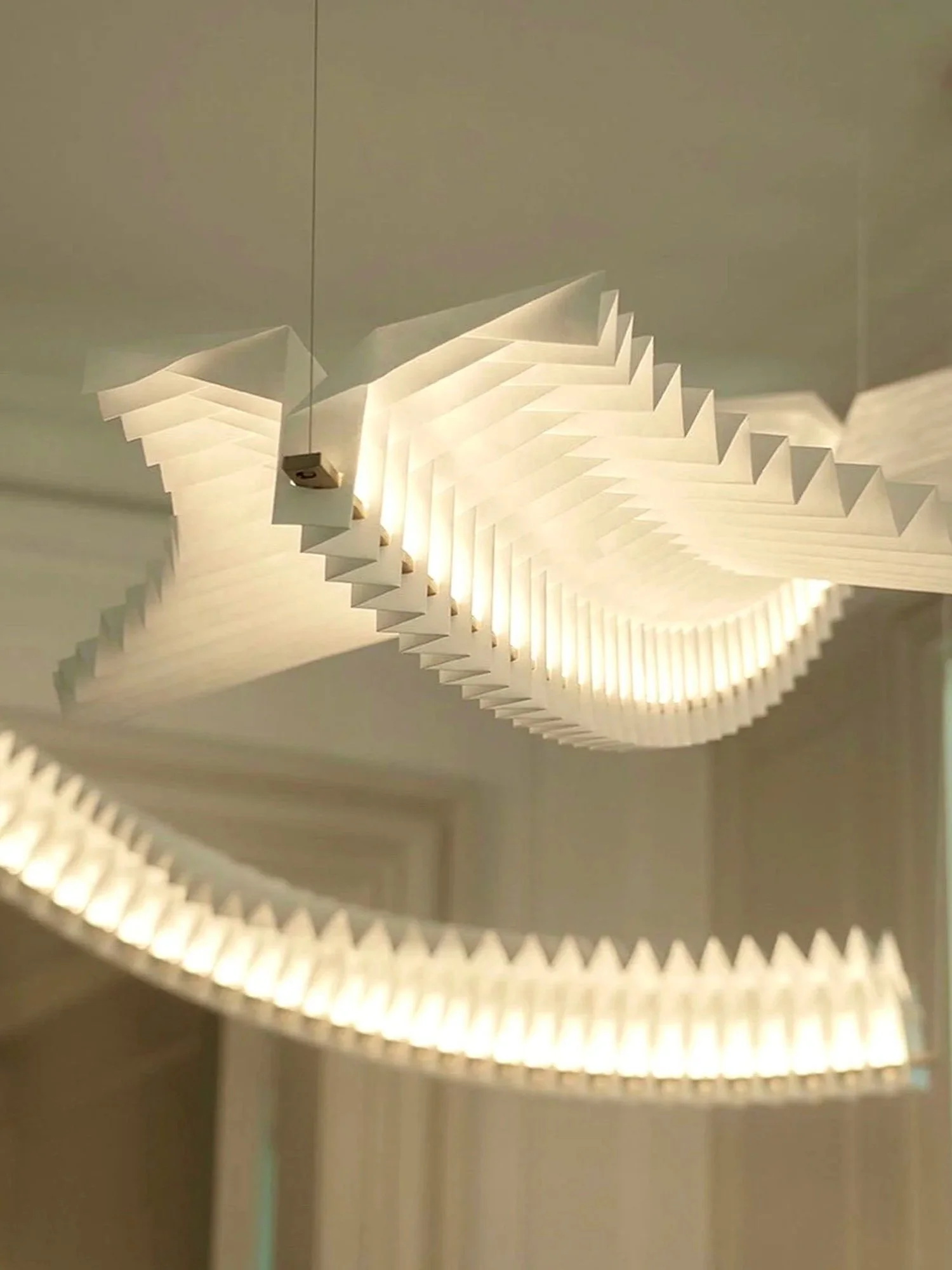 Modern white chandelier with layered, wavy design hanging from ceiling.
