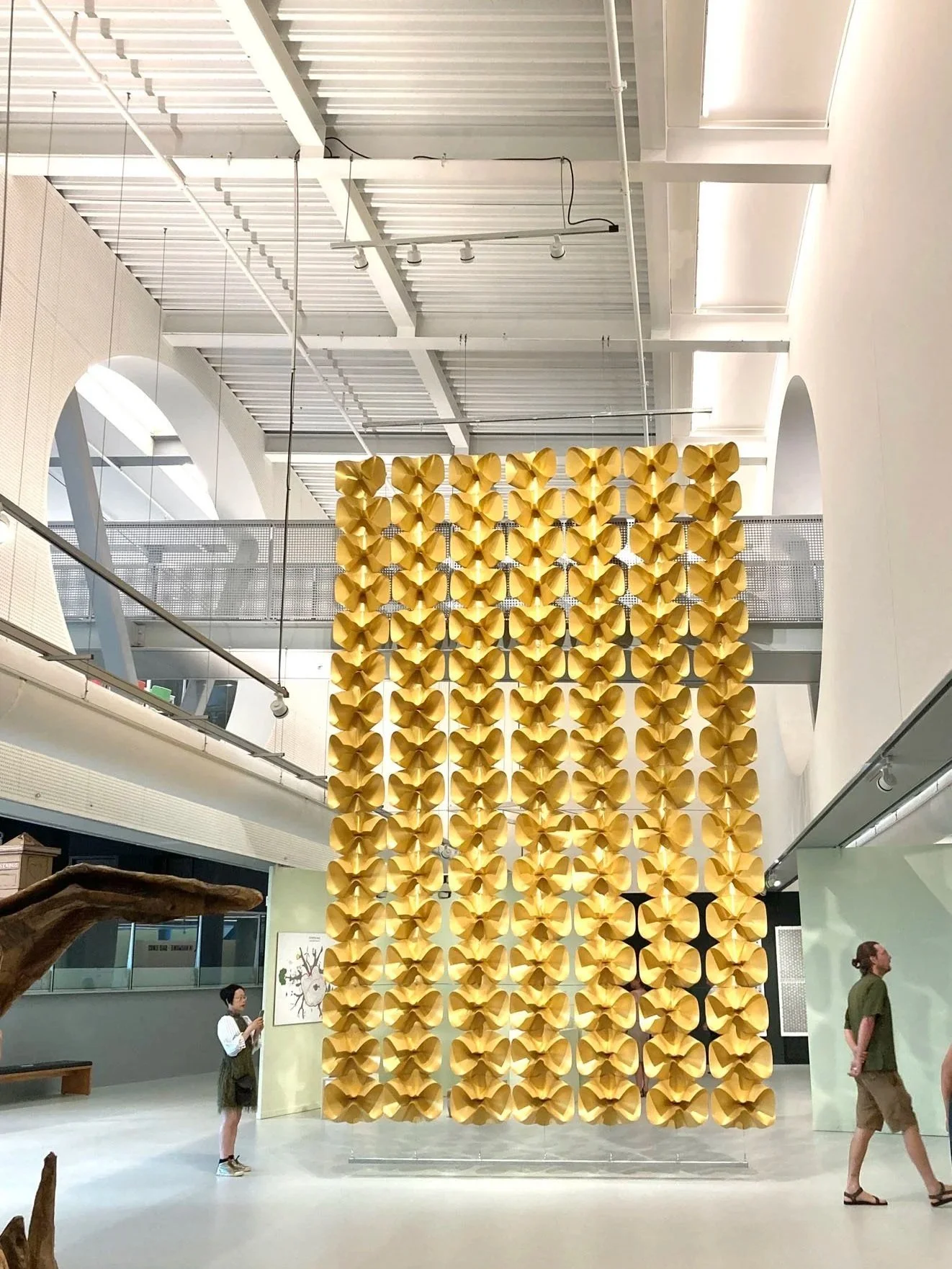 Large yellow geometric wall sculpture in art gallery with visitors observing.