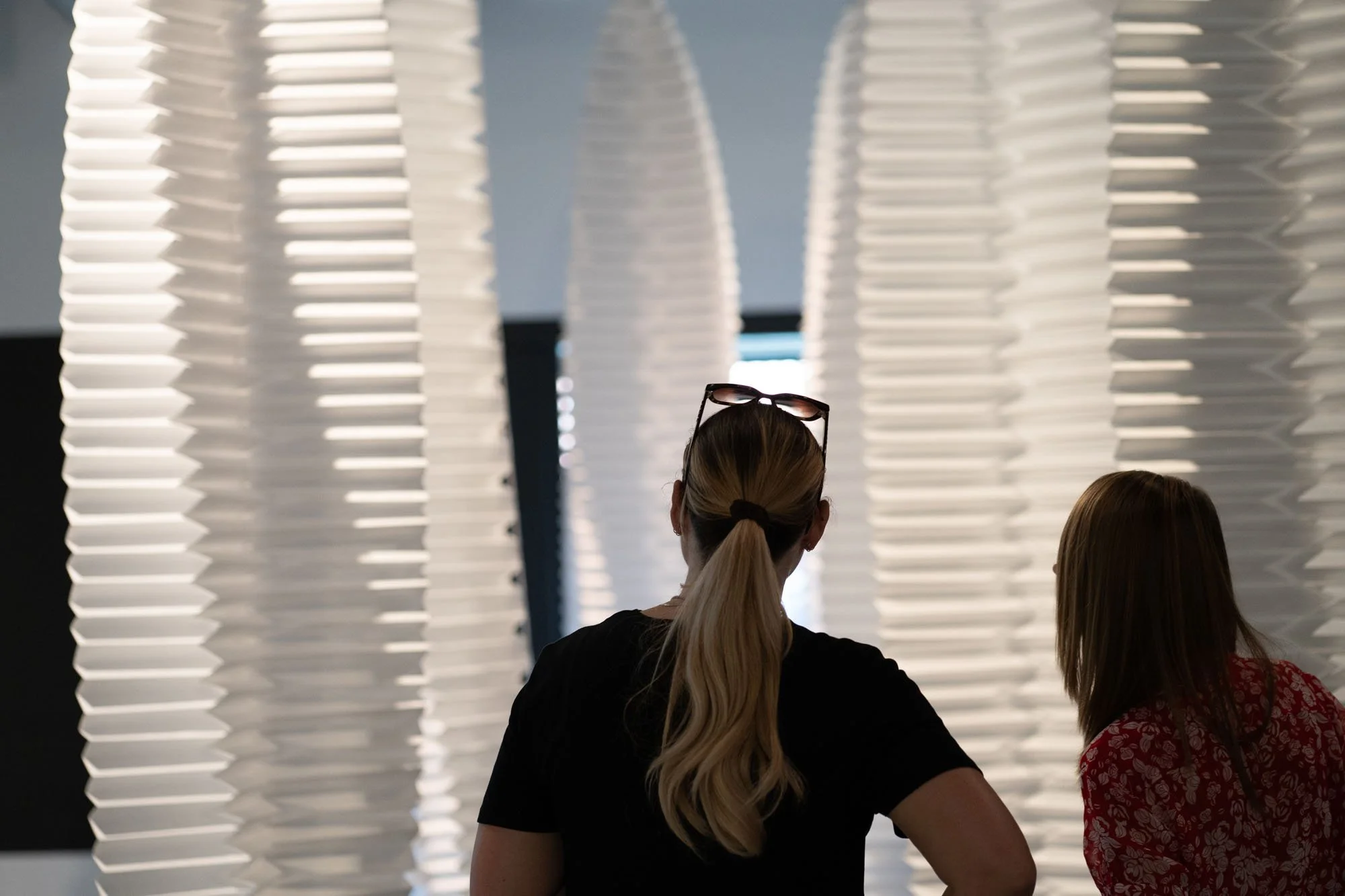Two women viewing an art installation with white, zigzag-patterned panels that create a tunnel effect.