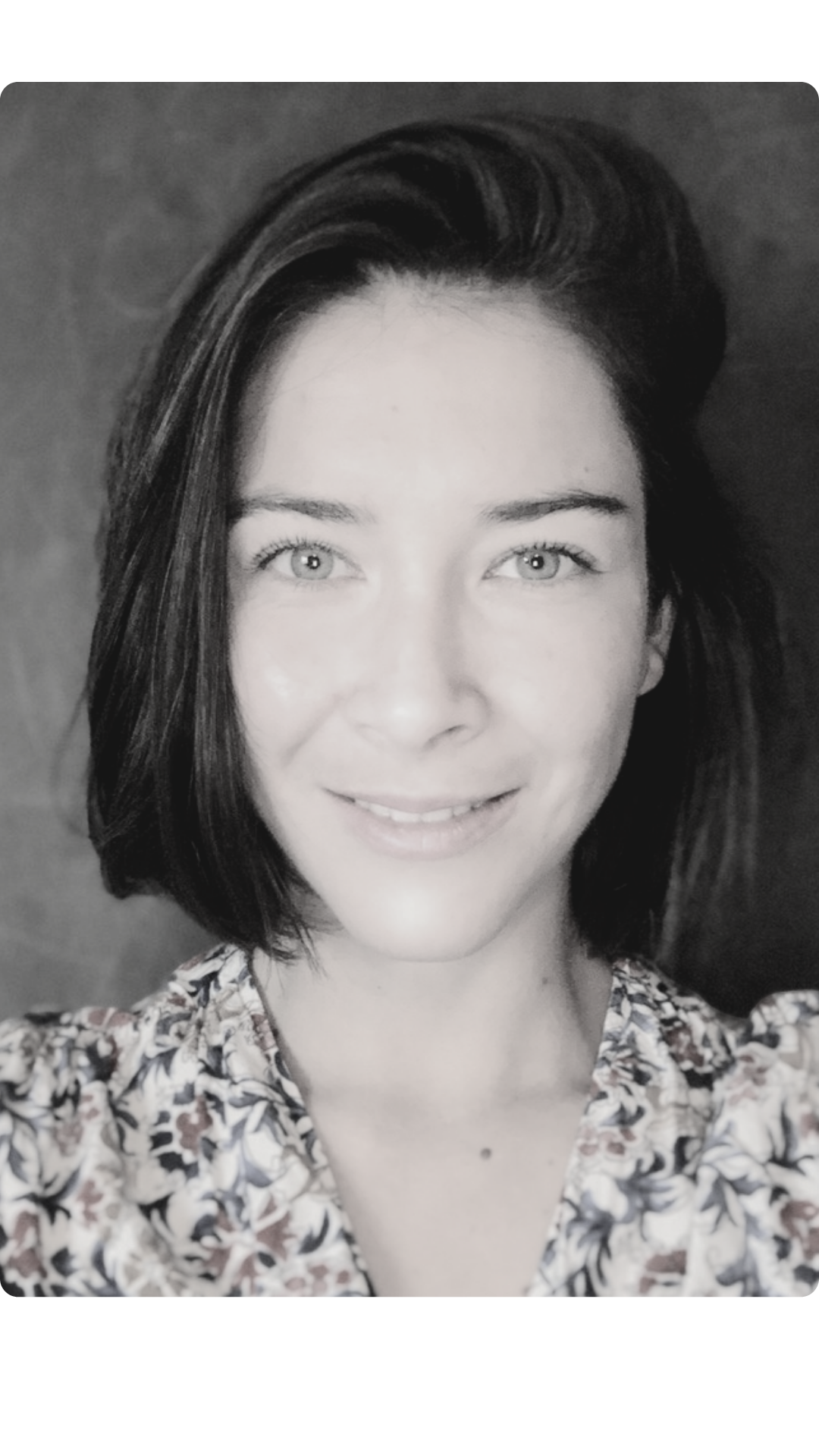 Portrait en noir et blanc d'une femme souriante avec des cheveux courts et des yeux clairs, portant une chemise à motifs floraux.