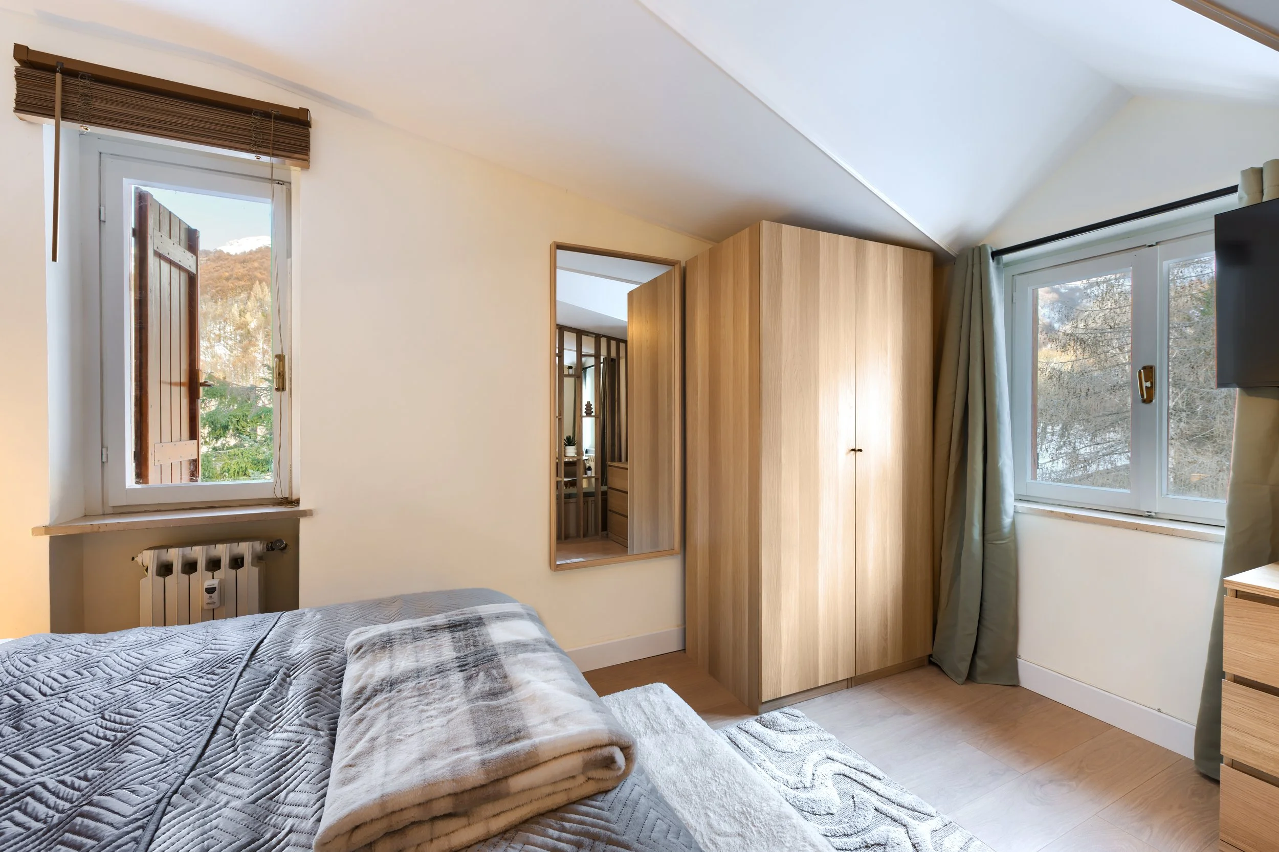 Bedroom with two windows, wooden wardrobe, mirror, bed with gray patterned blanket, and light wooden furniture, a luxurious retreat, an exclusive retreat, a refined mountain retreat, a premium alpine retreat.