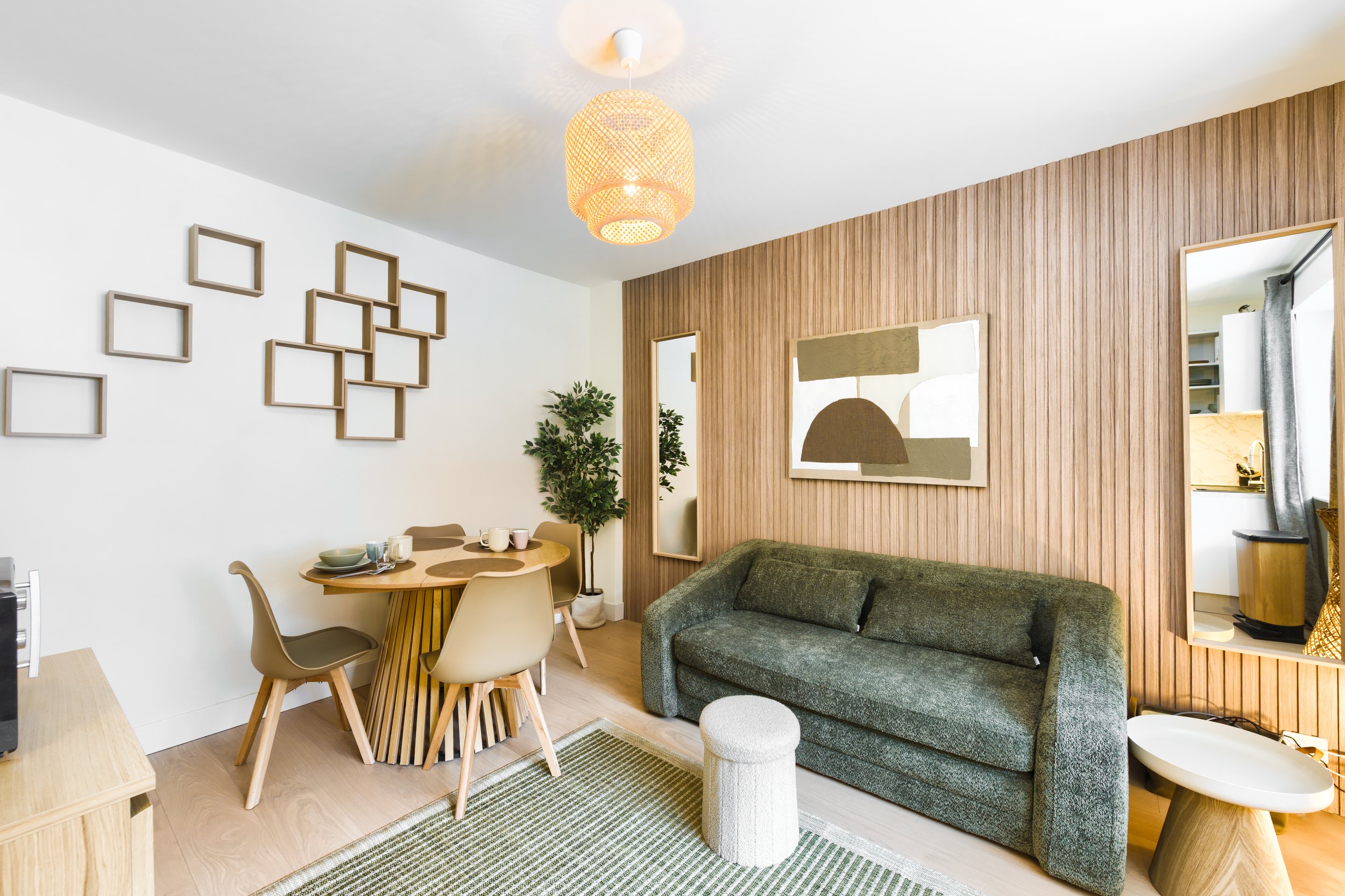 Modern living room with a green sofa, wooden wall paneling, abstract art, dining area with beige chairs, and a wooden dining table, decorated with plants and framed wall art, a luxurious retreat, an exclusive retreat, a refined mountain retreat. 