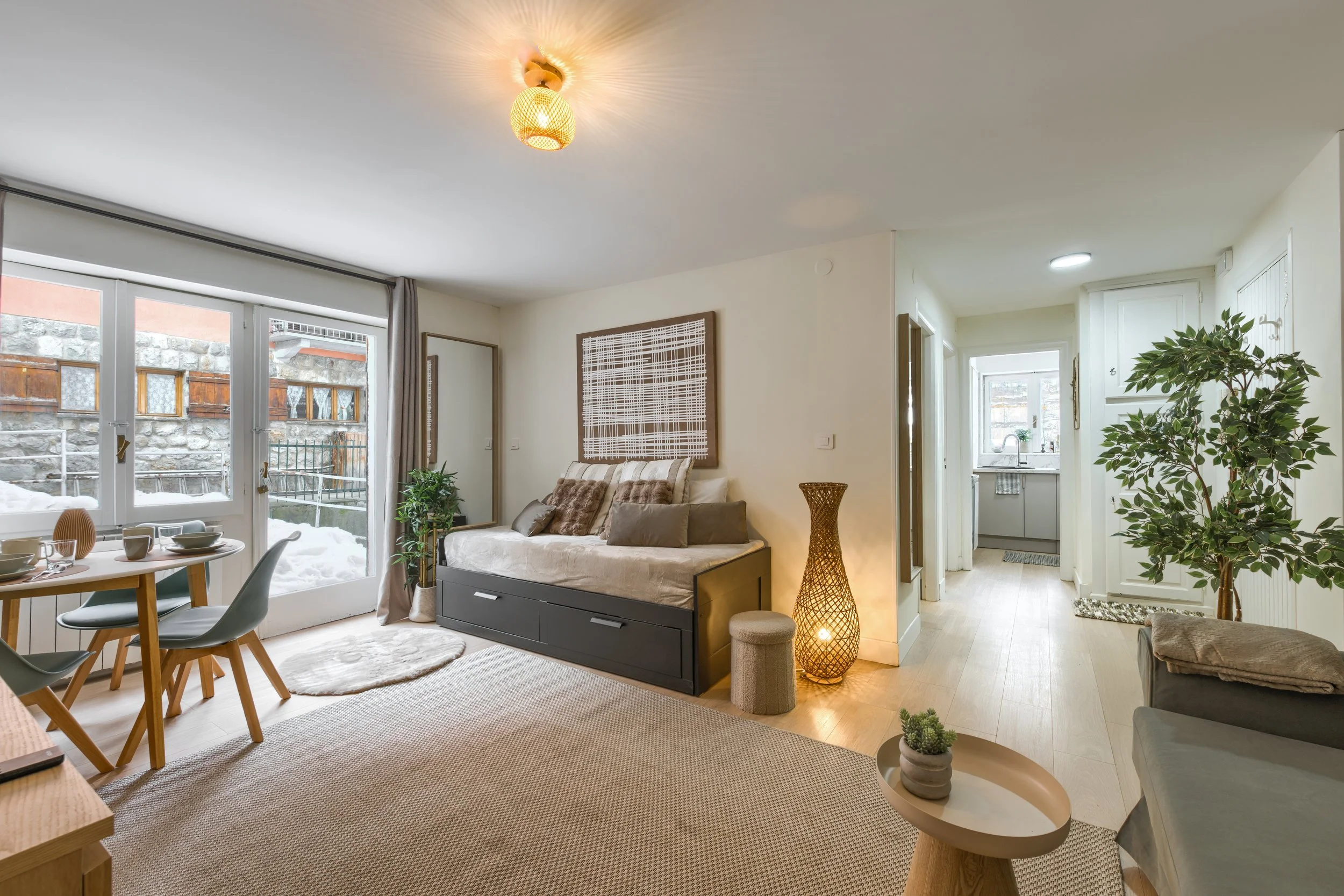 Living room with a daybed, dining table, and plants, leading to a snow-covered outdoor patio through glass doors, a luxurious retreat, an exclusive retreat, a refined mountain retreat, a premium alpine retreat.