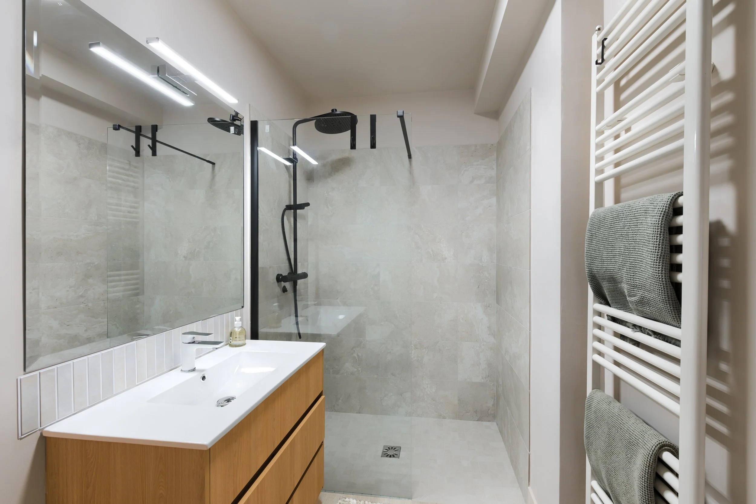 Modern bathroom with walk-in shower, wooden vanity with sink, large mirror, and wall-mounted towel radiator with two towels, a luxurious retreat, an exclusive retreat, a refined mountain retreat, a premium alpine retreat.