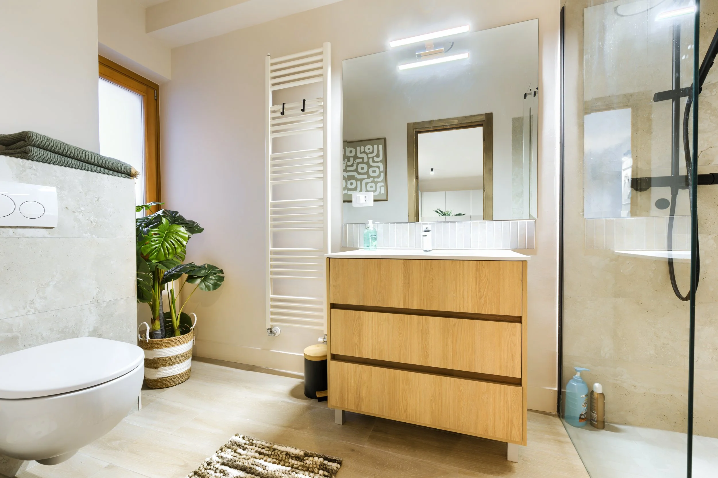 Modern bathroom with a wooden vanity, large mirror, walk-in shower, toilet, and a potted plant near a window, a luxurious retreat, an exclusive retreat, a refined mountain retreat, a premium alpine retreat.
