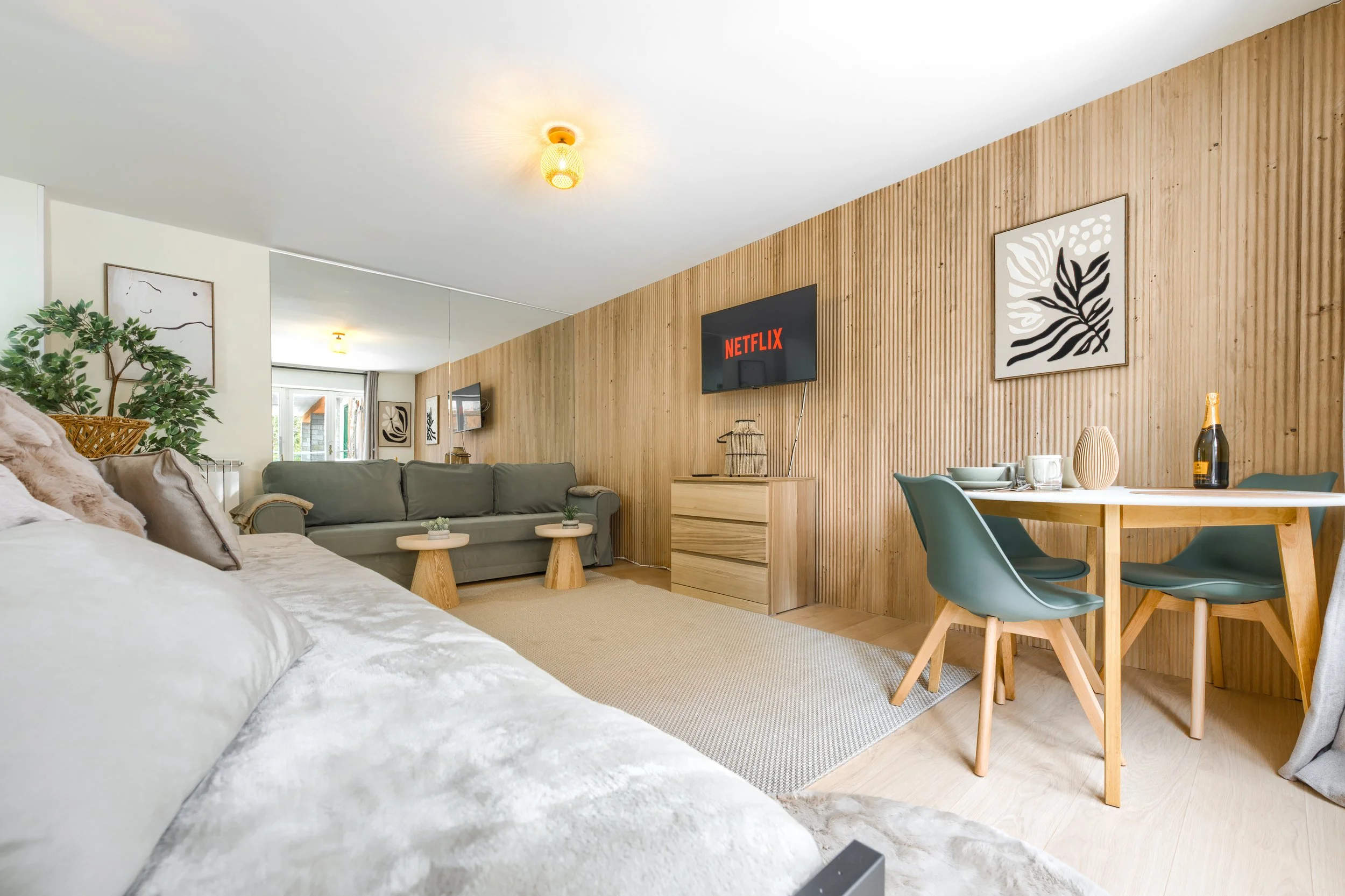 Living room with a gray couch, a television showing Netflix, and a dining area with four teal chairs and a wooden table, decorated with artwork and plants, a luxurious retreat, an exclusive retreat, a refined mountain retreat, premium alpine retreat.