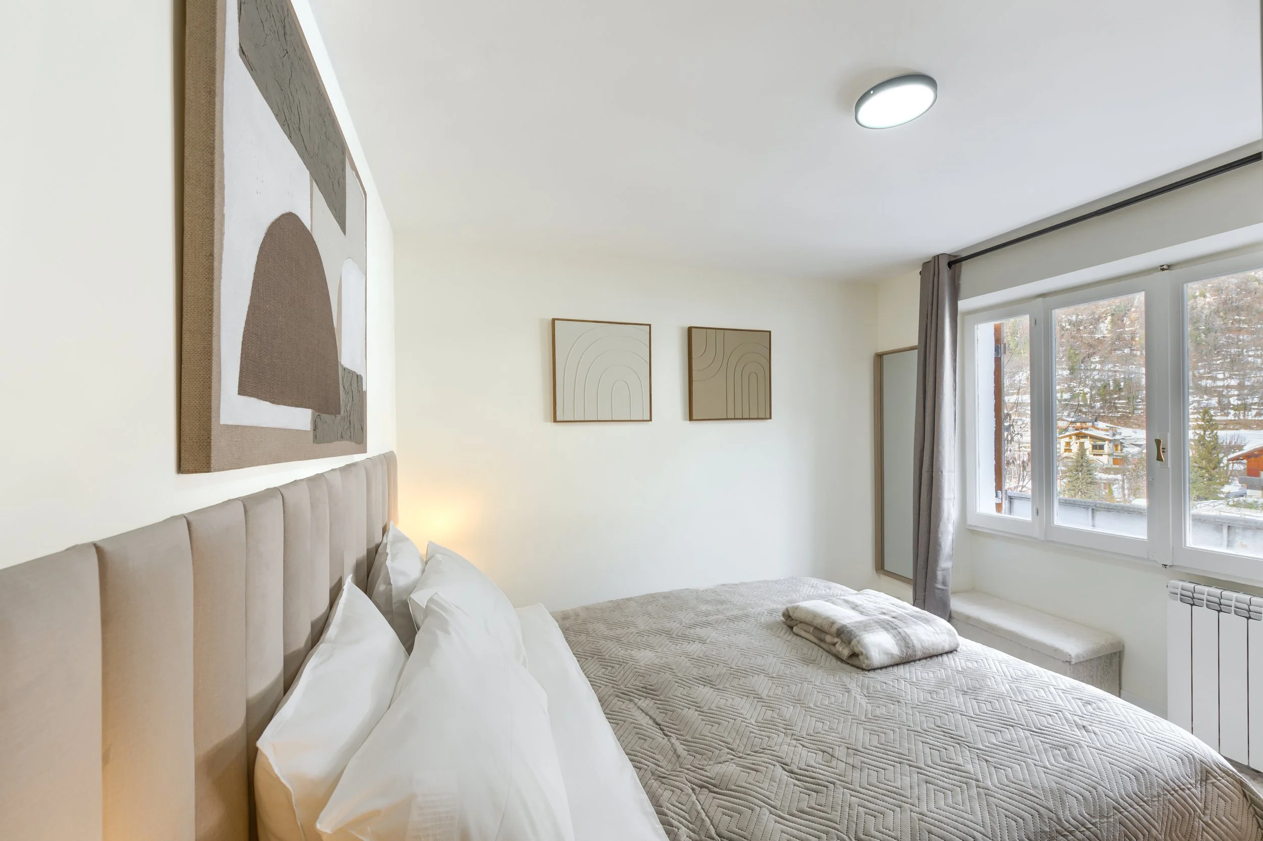 A bedroom with a bed, white pillows, beige headboard, wall art, window with curtains, and a blanket on the bed, a luxurious retreat, an exclusive retreat, a refined mountain retreat, a premium alpine retreat.