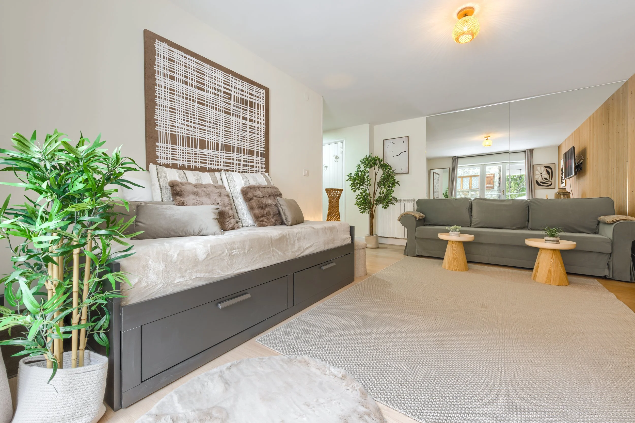 Living room with two sofas, one beige with cushions and a gray one, and a tall potted plant, wooden wall, artwork, window, and ceiling lights, a luxurious retreat, an exclusive retreat, a refined mountain retreat, a premium alpine retreat.