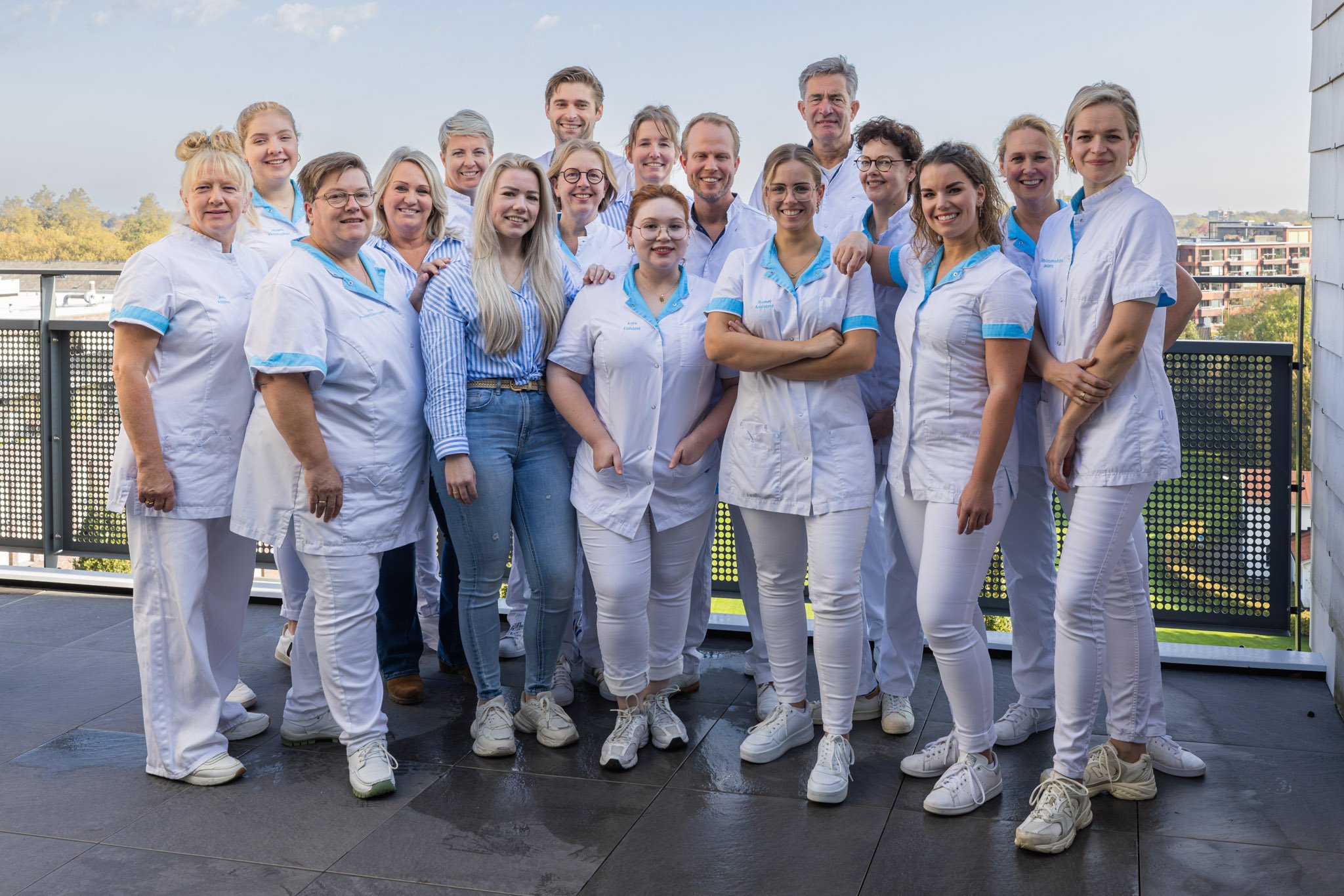 A group of healthcare professionals on a balcony, dressed in white and light blue uniforms, smiling.