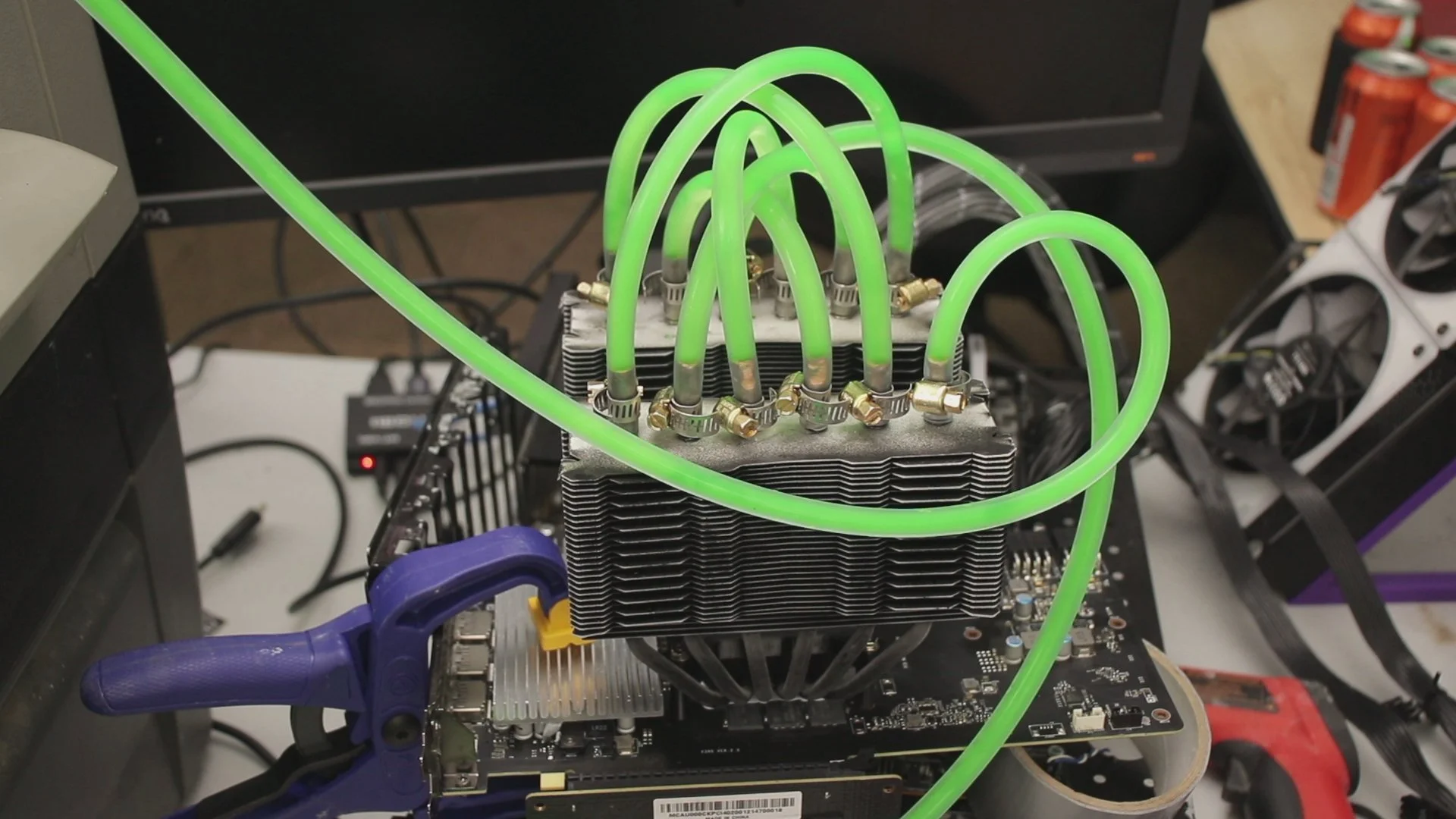A computer graphics card with a large heat sink and multiple neon green liquid cooling tubes connected to it, setup for custom water cooling.