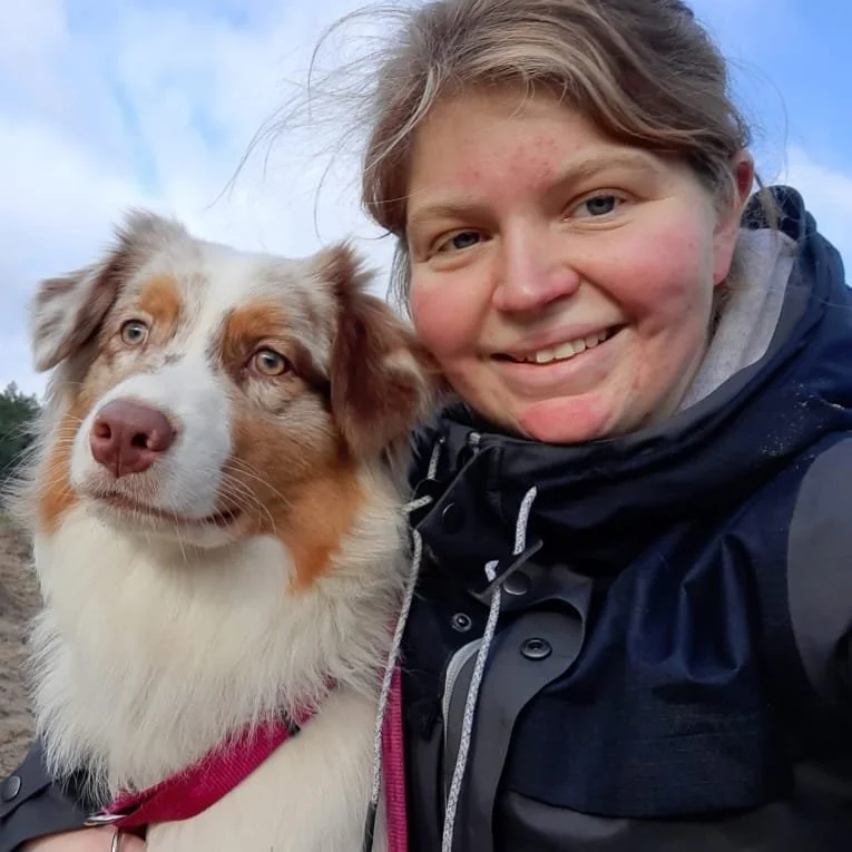 Een vrouw die blij is, poseert met haar Australië herder hond buiten tijdens een dagwandeling.