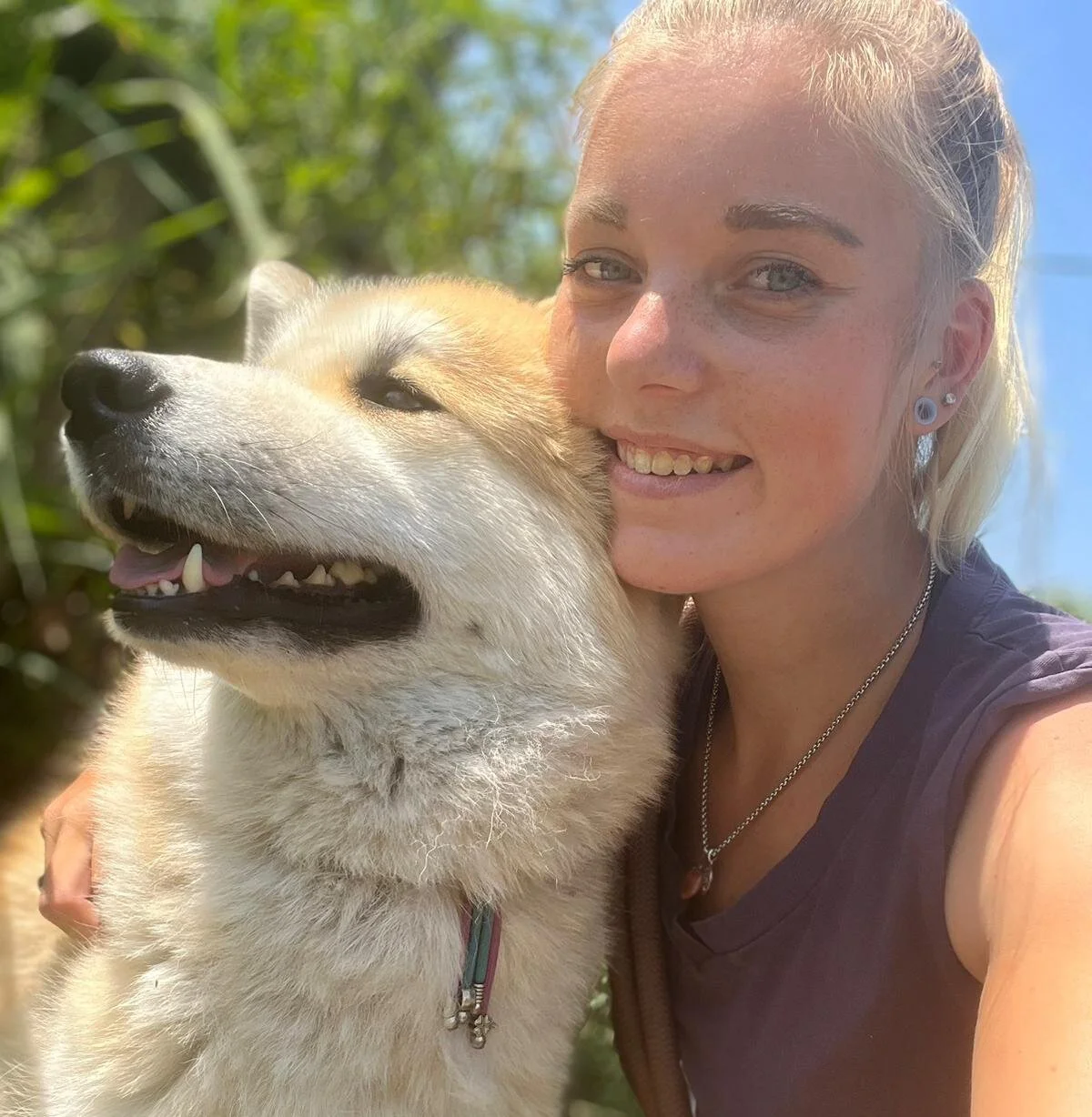 Een vrouw met een glimlach om haar gezicht die knuffelt met een blije, whitish-geel hond.