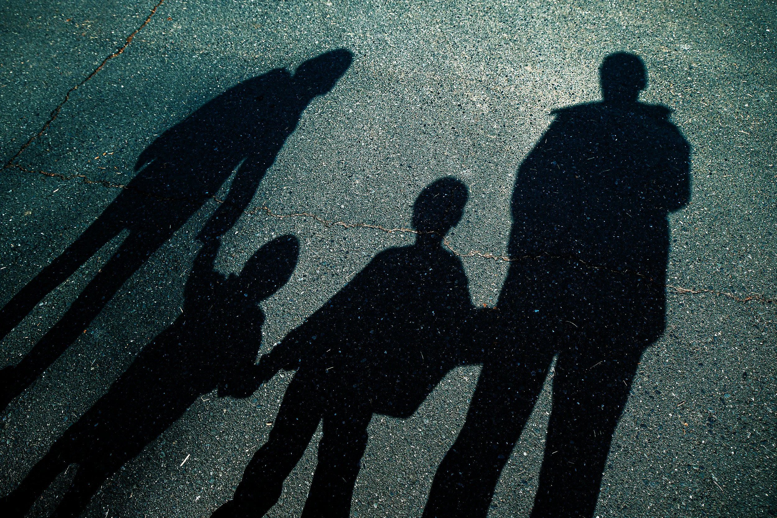 Shadows of three people, including an adult man, a woman, and a child, holding hands and walking on an asphalt surface.