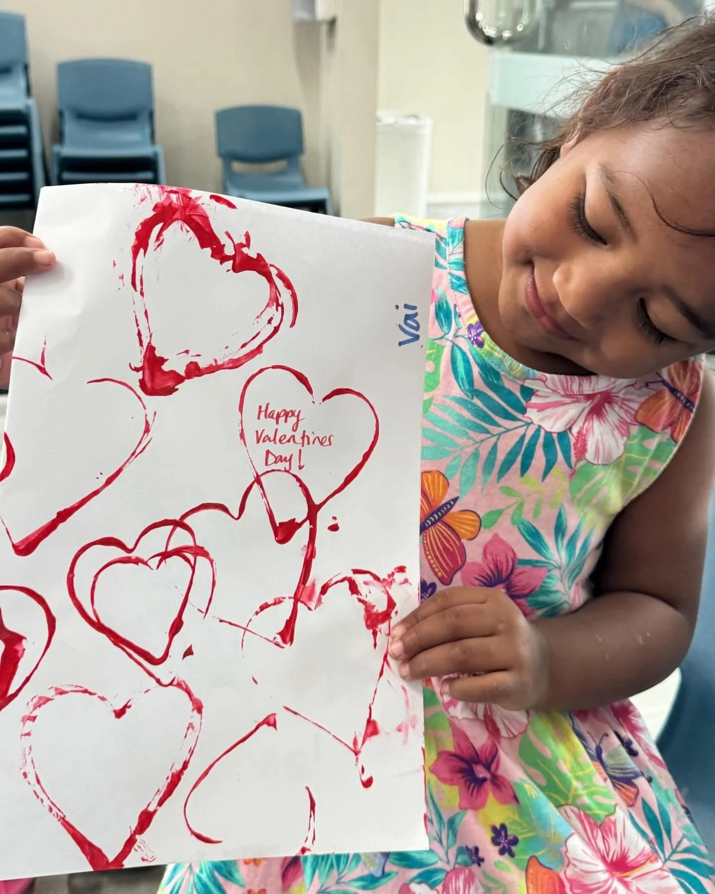 Young girl holding a handmade Valentine's Day card with red heart drawings and the message 'Happy Valentine's Day!' written inside one of the hearts. Children doing arts and crafts experience. Henderson community.