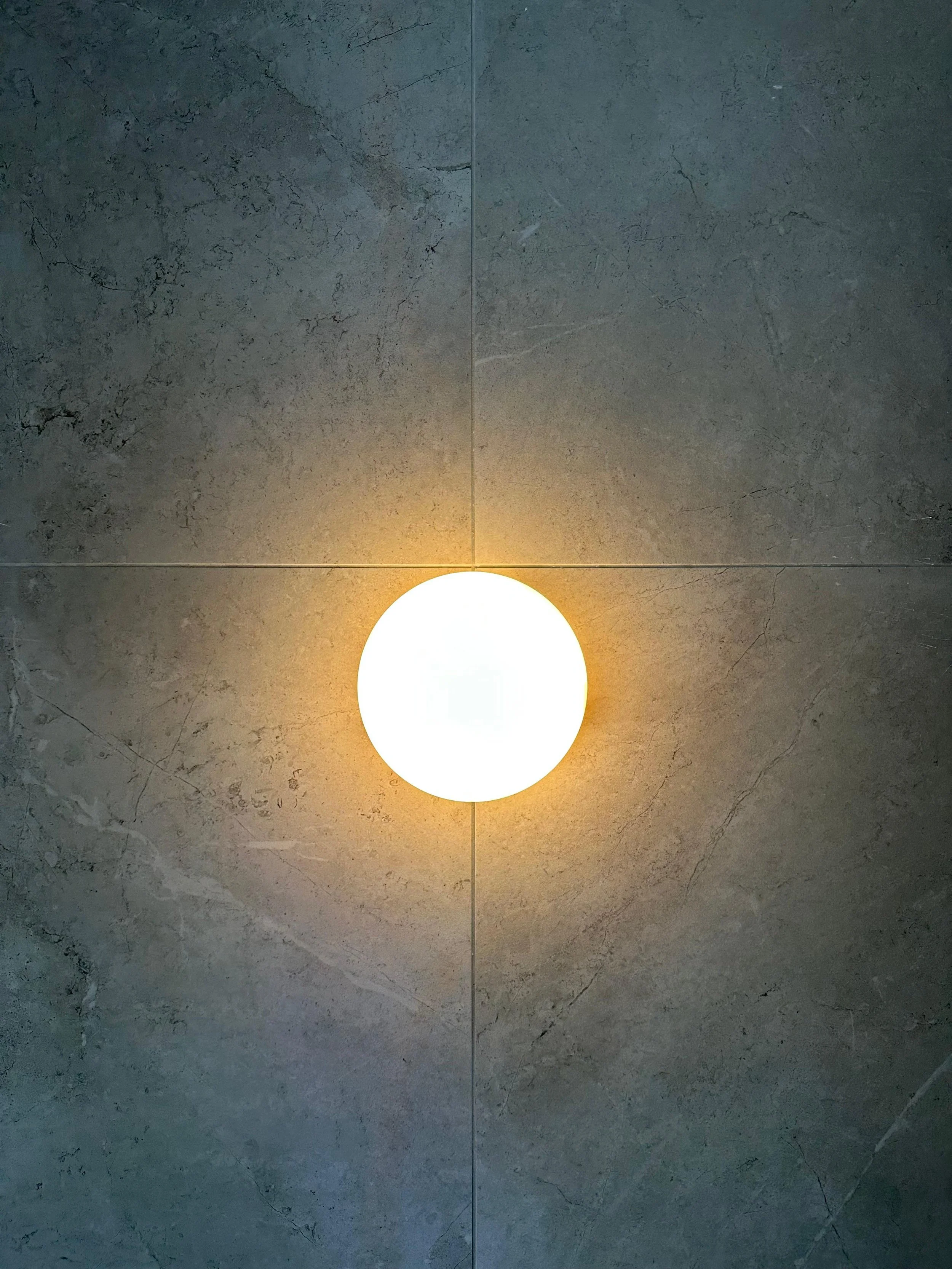 Ceiling light fixture with glowing white orb and warm ambient glow on gray marble ceiling.