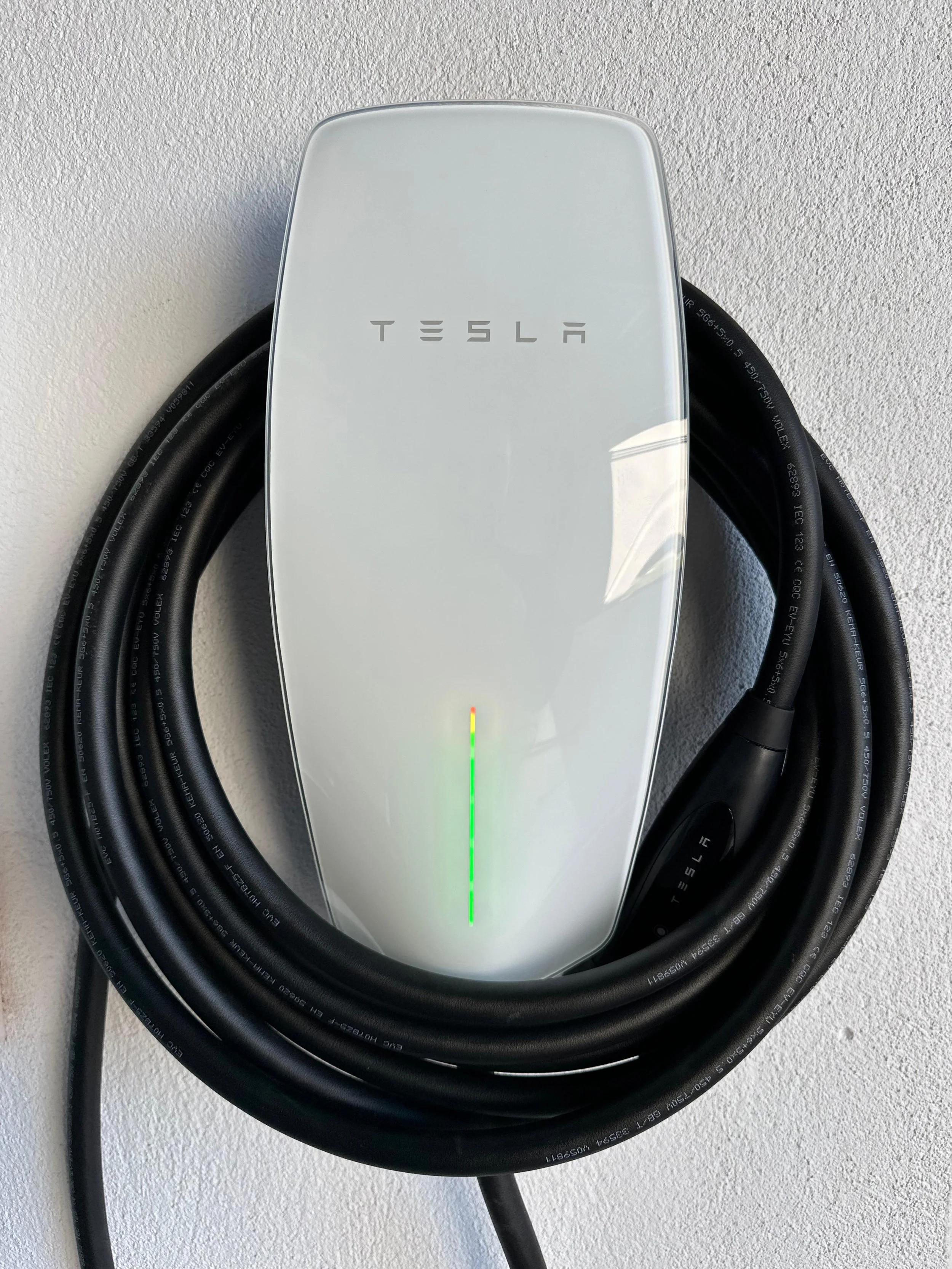 Tesla electric vehicle wall charger mounted on a wall with a coiled black cable.