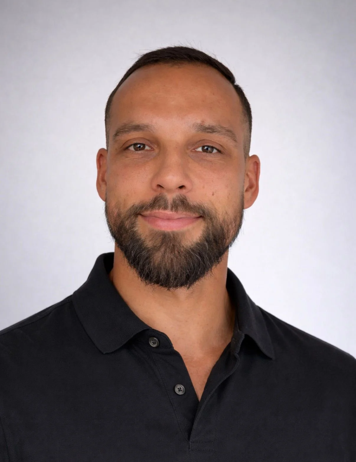 Headshot of a smiling man with short dark hair and beard, wearing a black collared shirt against a plain light background.