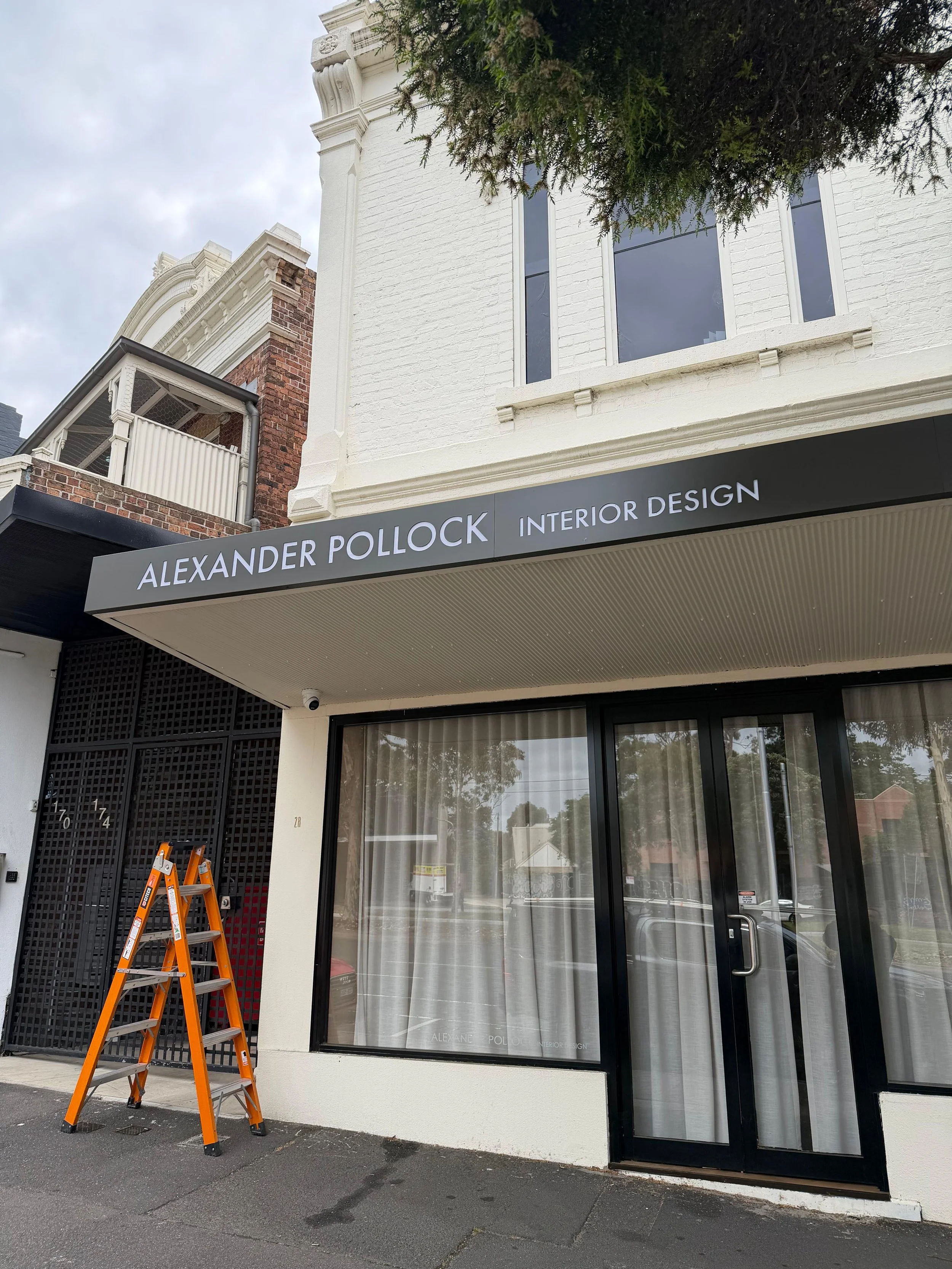  storefront with sign reading "ALEXANDER POLLOCK INTERIOR DESIGN" and an orange ladder on the sidewalk in front