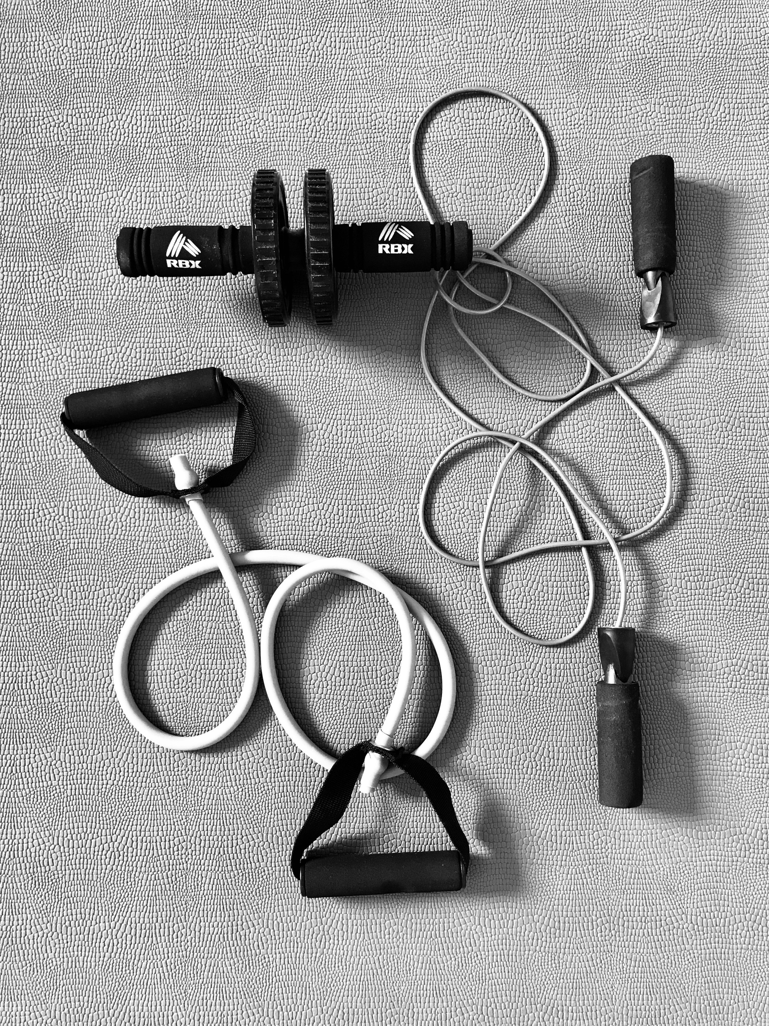 Black and white exercise equipment on textured surface, including jump rope, hand grip, ab roller, and push-up bars.