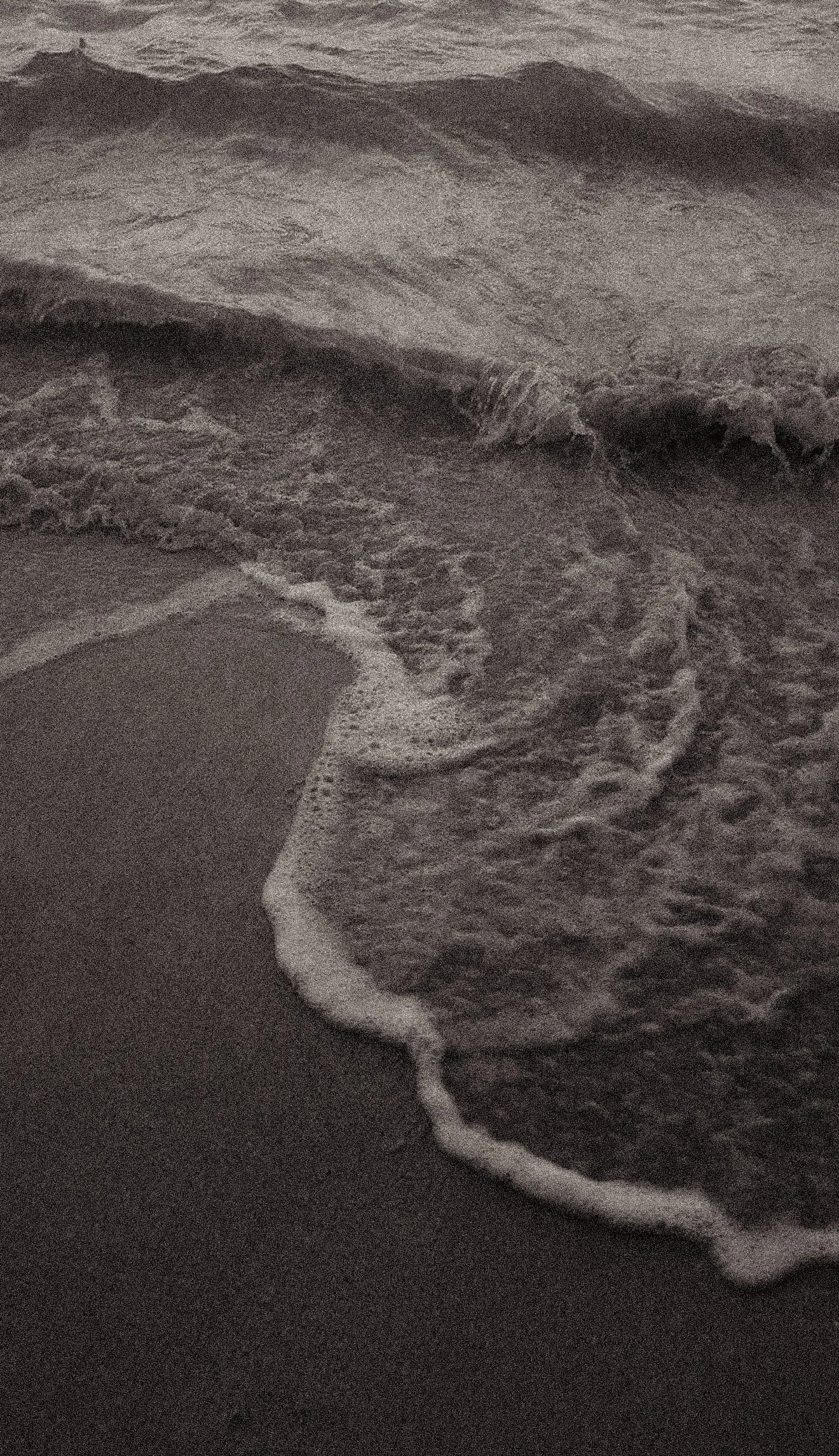 Waves crashing onto a sandy beach at dusk or dawn.
