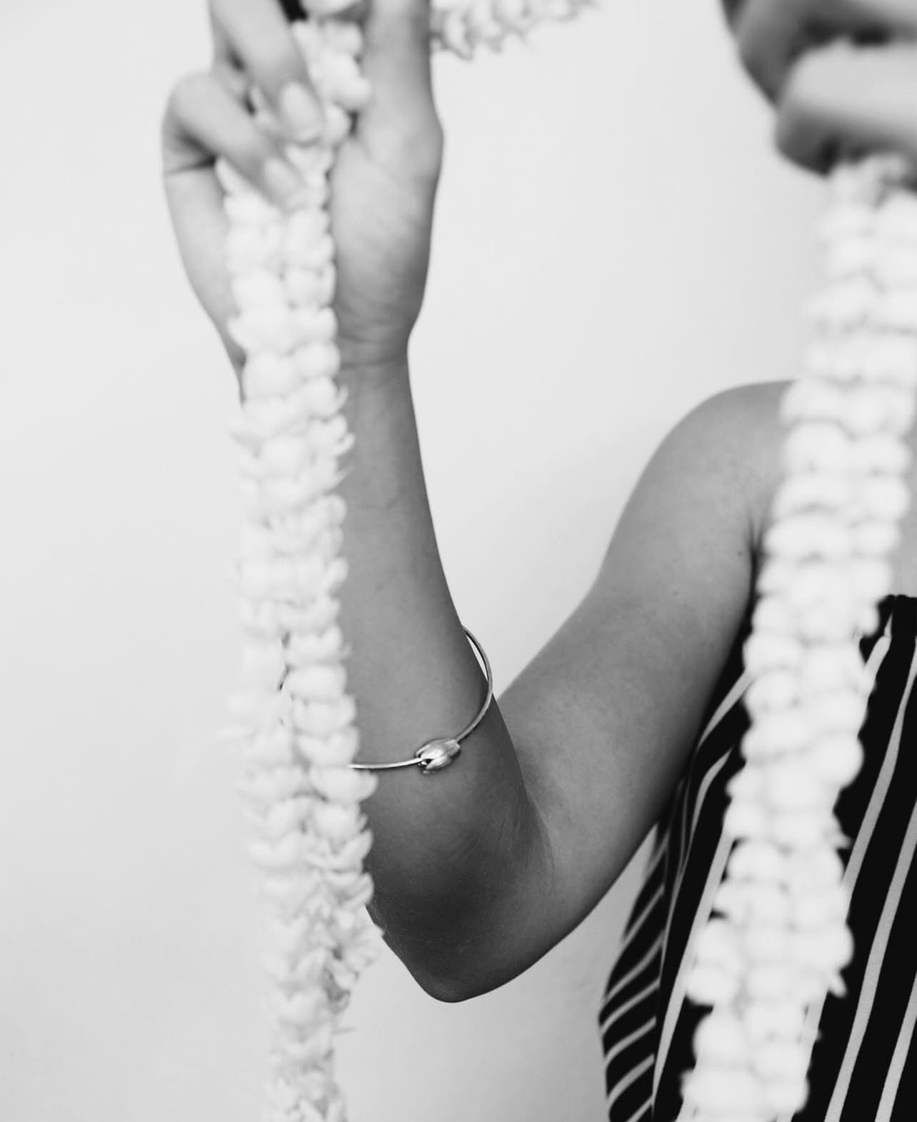 A person holding a string of paper flowers, wearing a striped sleeveless top and a bracelet.