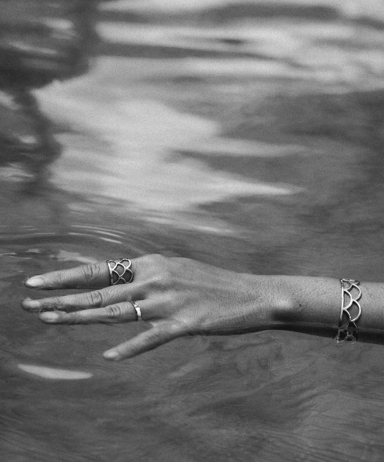 A pair of hands with rings and bracelets partially submerged in water.