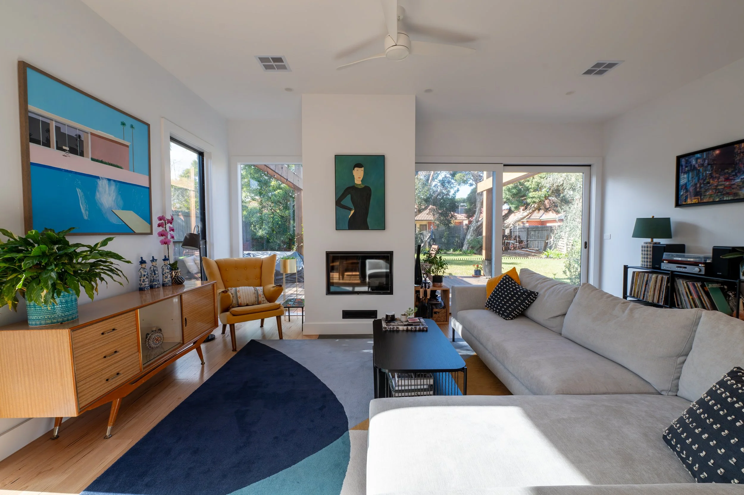 Oak Street Project lounge room with a fireplace, opening to the rear deck and backyard through large openings