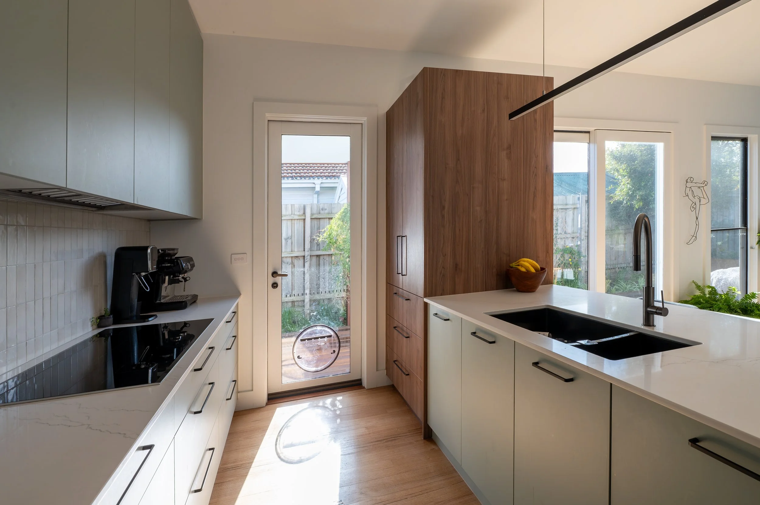 Side view of the Oak Street Project kitchen showing flow to the outdoor BBQ area and an appliances cupboard that doubles as a bookshelf facing the dining area.